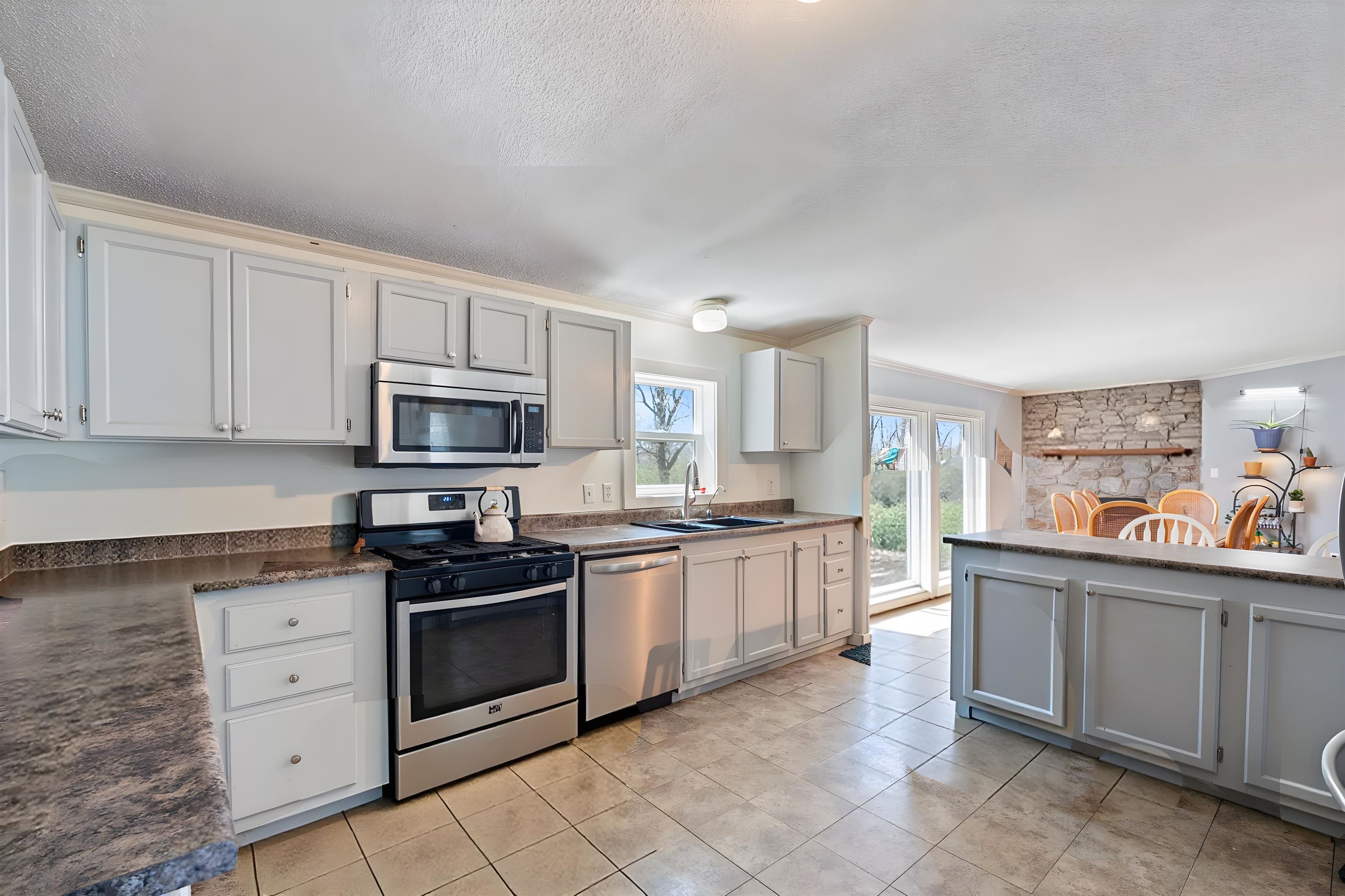 Kitchen featuring stainless steel appliances, dark countertops, light tile patterned floors, crown molding, and a textured ceiling