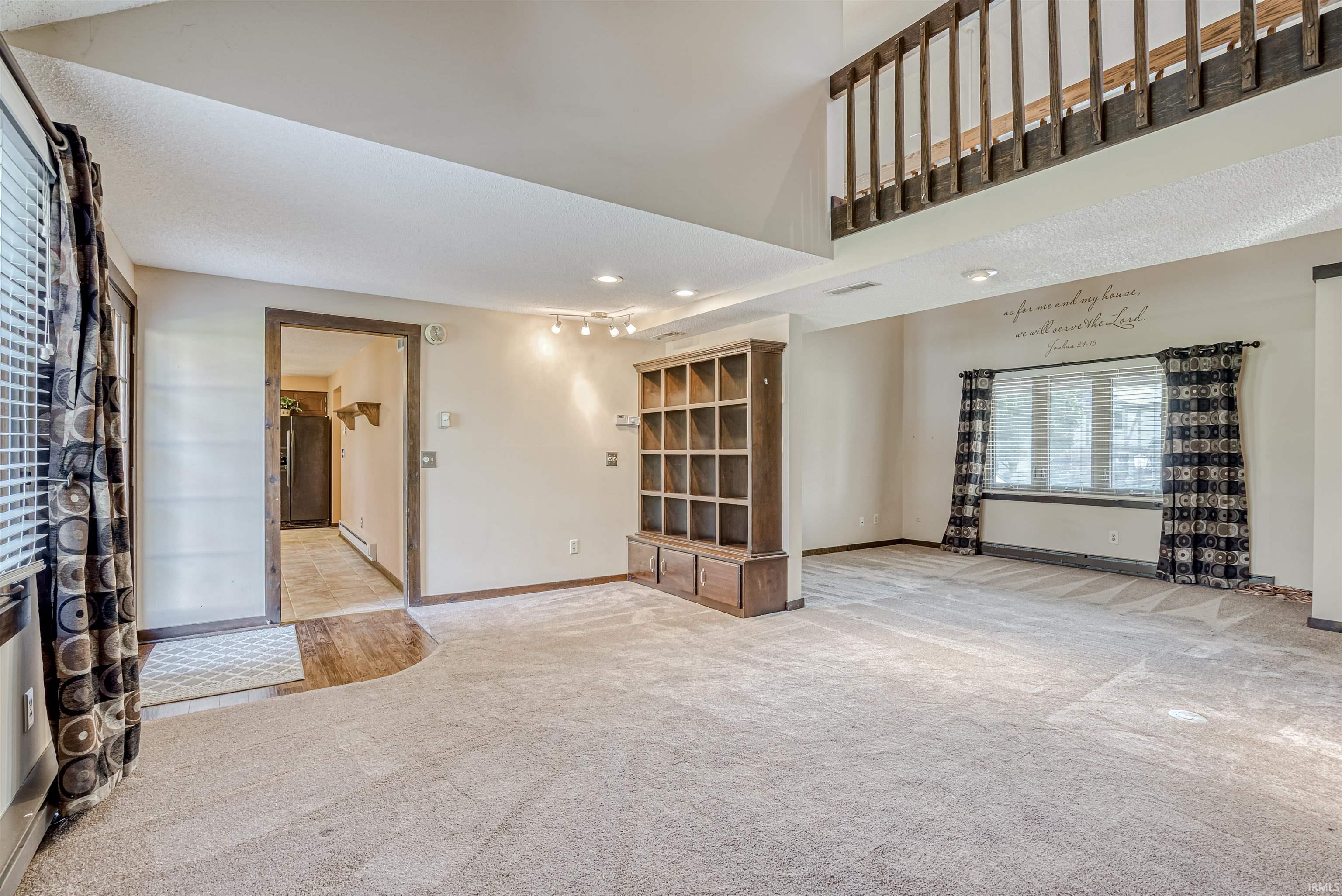 Unfurnished living room with light carpet, baseboard heating, recessed lighting, and a high ceiling