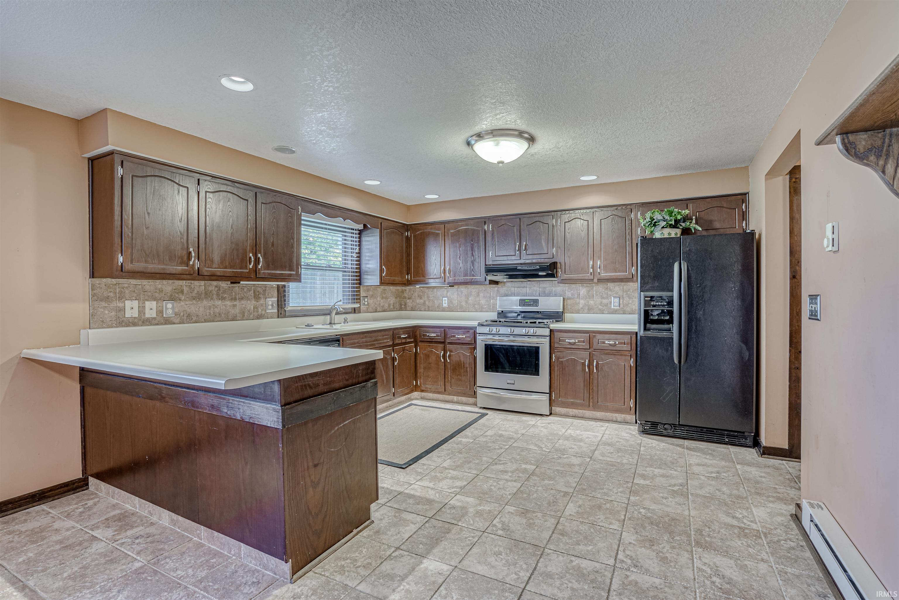Kitchen with black refrigerator with ice dispenser, tasteful backsplash, gas range, a baseboard heating unit, and a textured ceiling