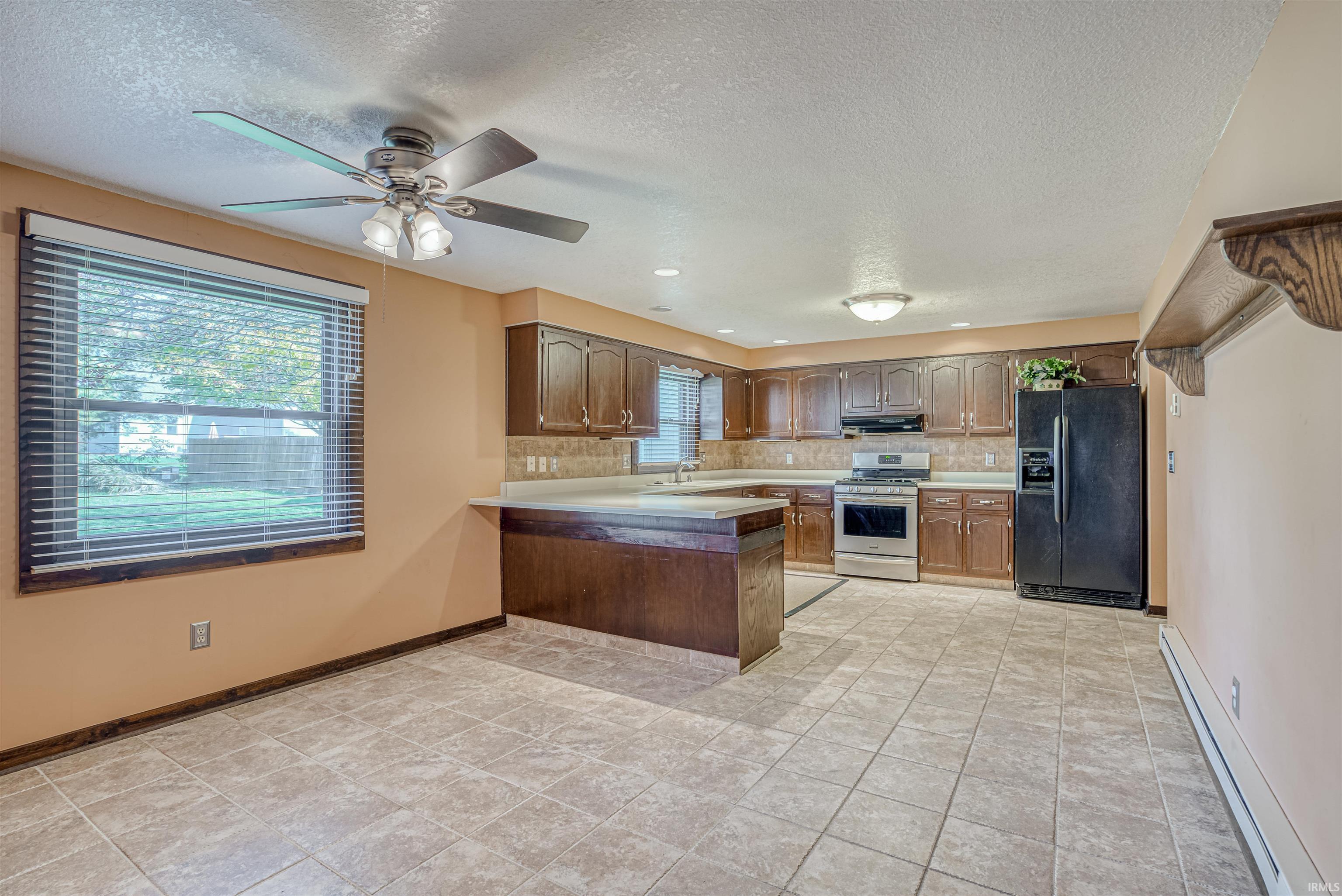 Kitchen featuring a baseboard heating unit, black refrigerator with ice dispenser, a peninsula, light countertops, and stainless steel gas range