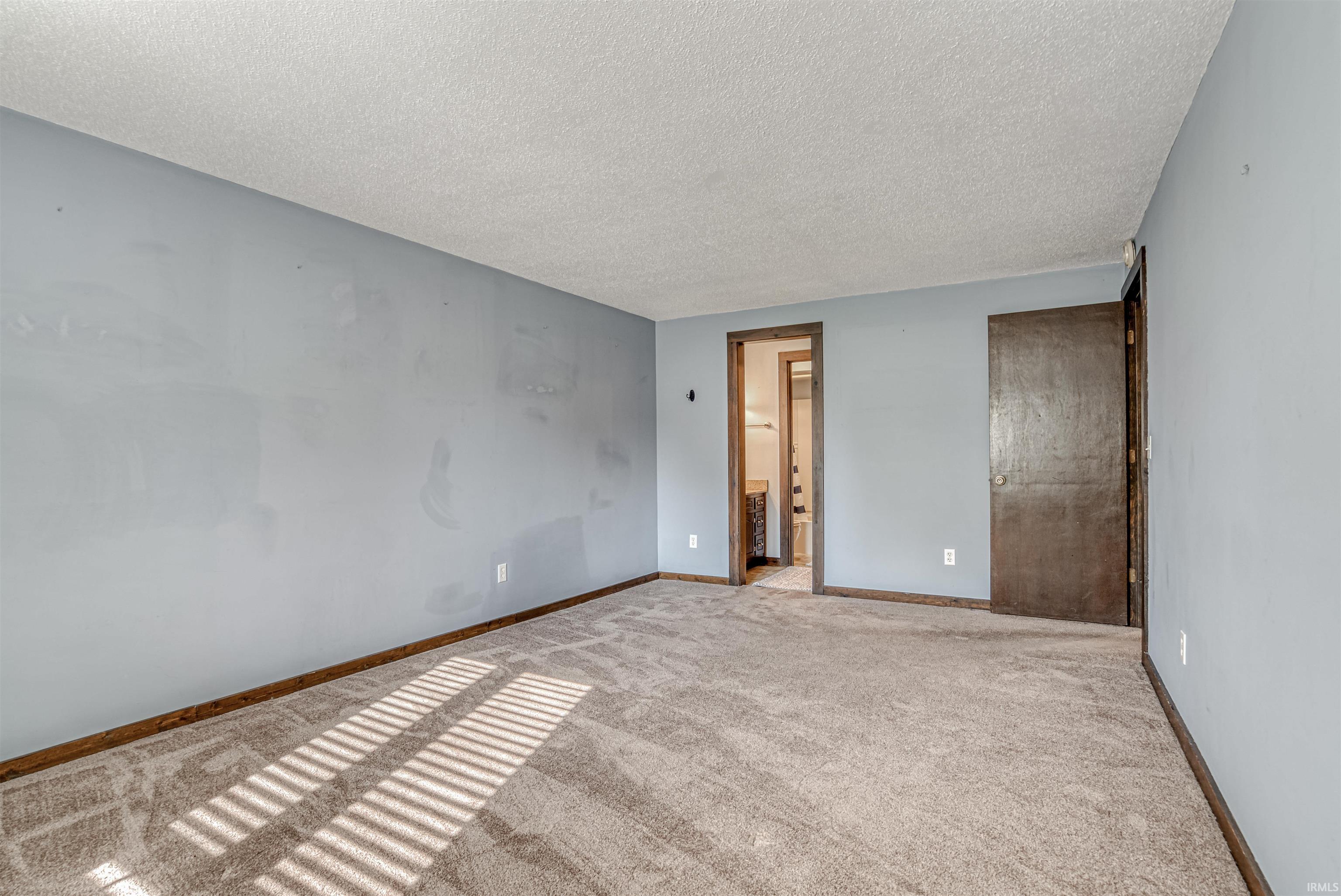 Unfurnished bedroom with a textured ceiling, light colored carpet, and connected bathroom