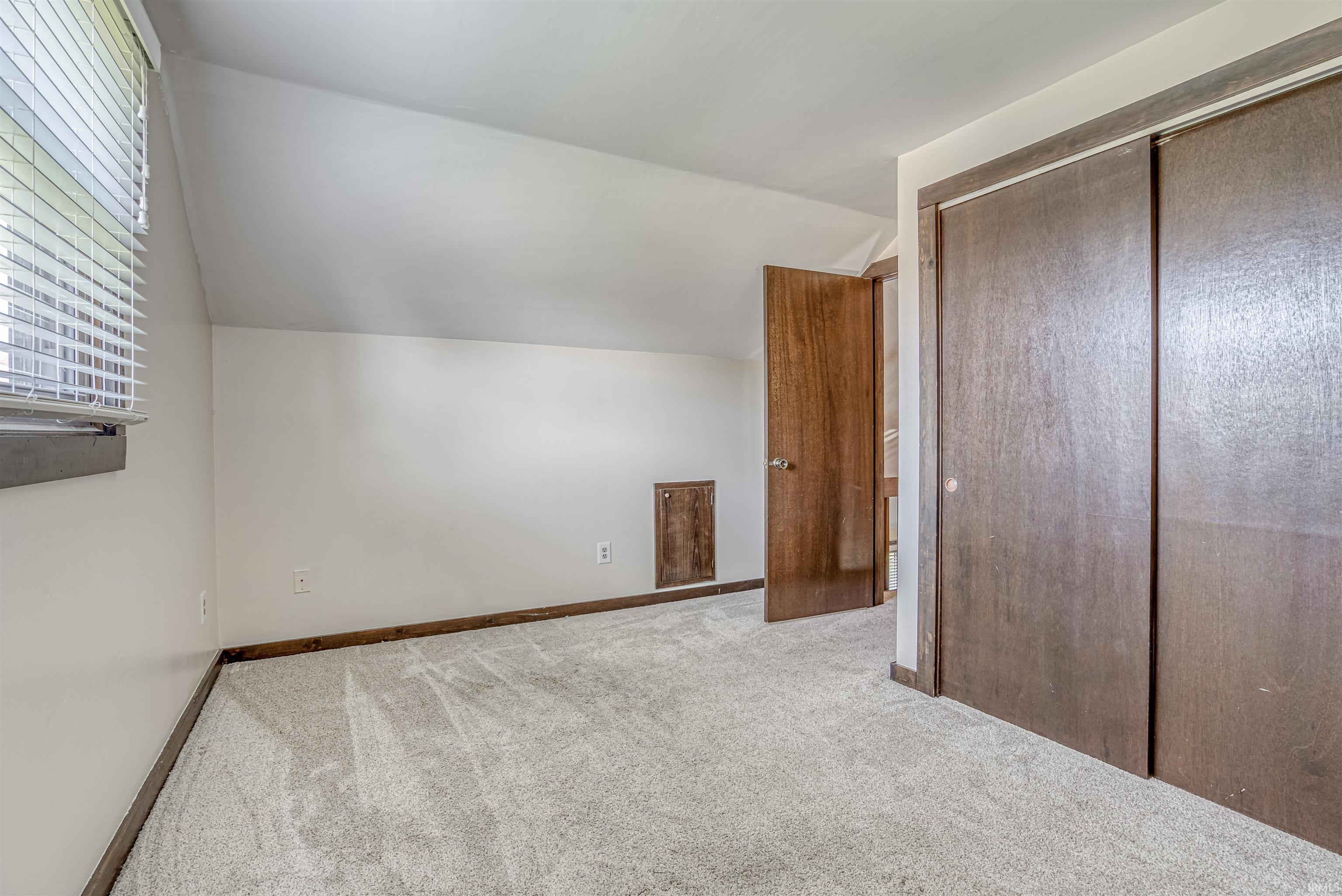 Unfurnished bedroom featuring lofted ceiling, light colored carpet, and a closet