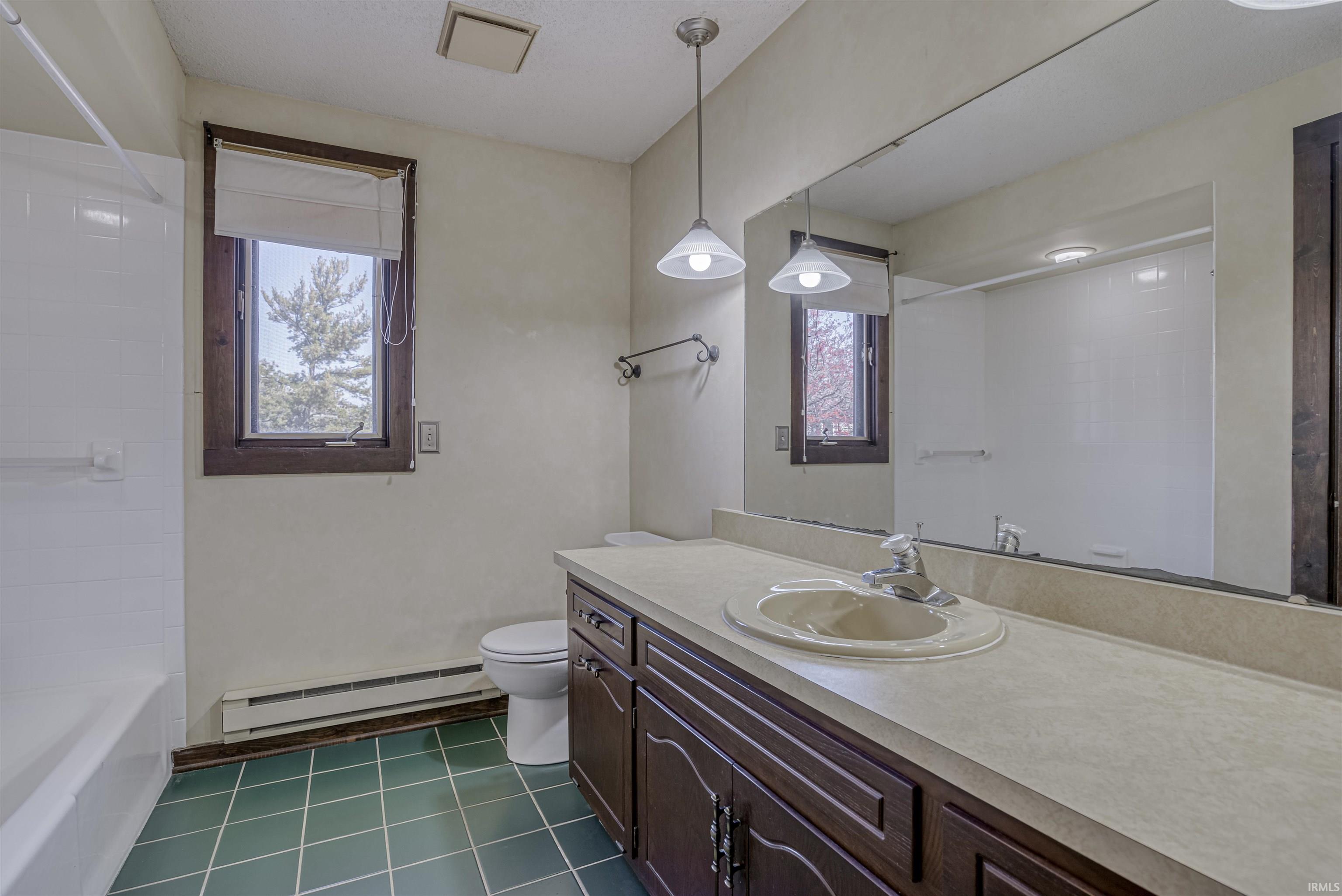 Bathroom with vanity, baseboard heating, dark tile patterned floors, and shower / bathtub combination