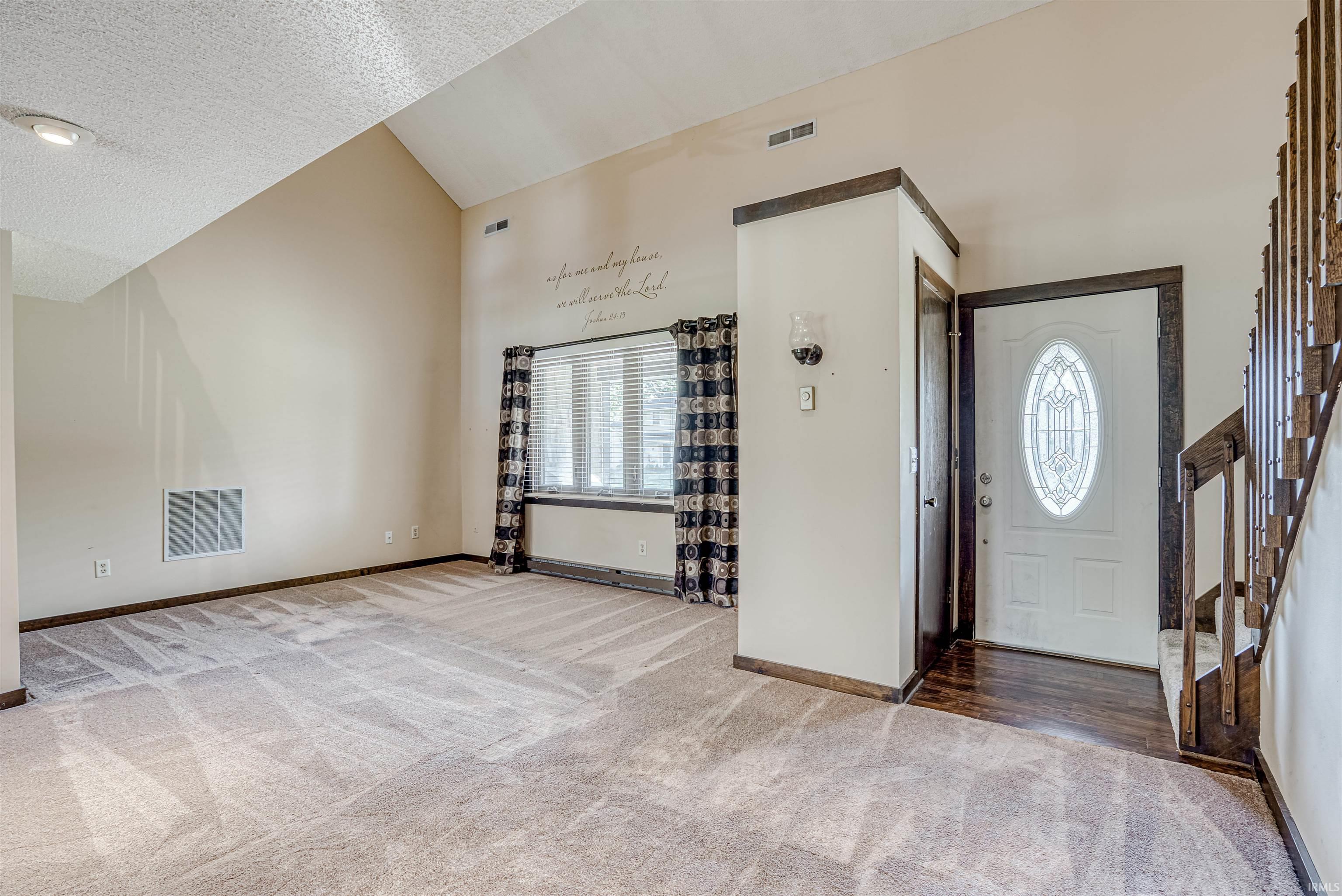 Foyer entrance with light colored carpet, plenty of natural light, and a high textured ceiling