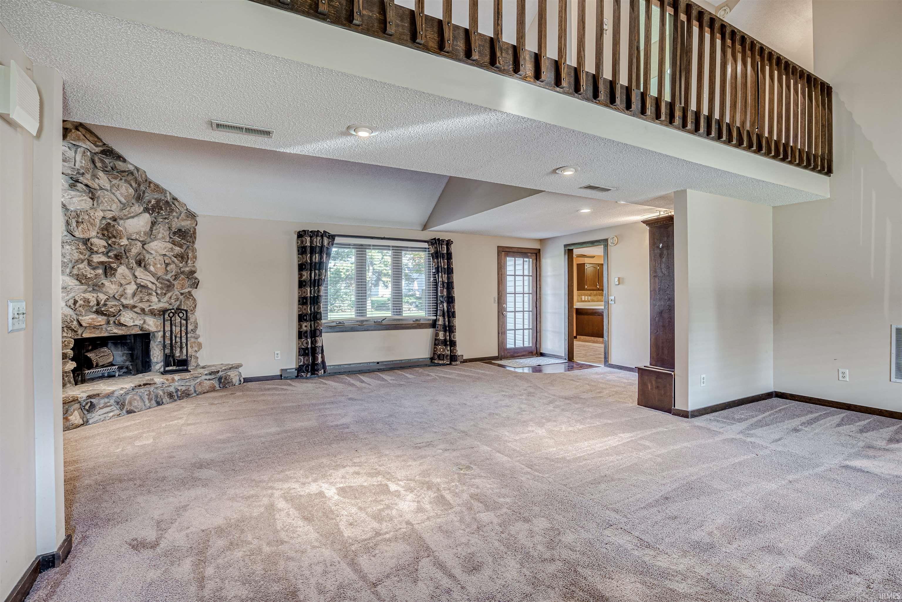 Unfurnished living room with light colored carpet, a fireplace, and a high textured ceiling