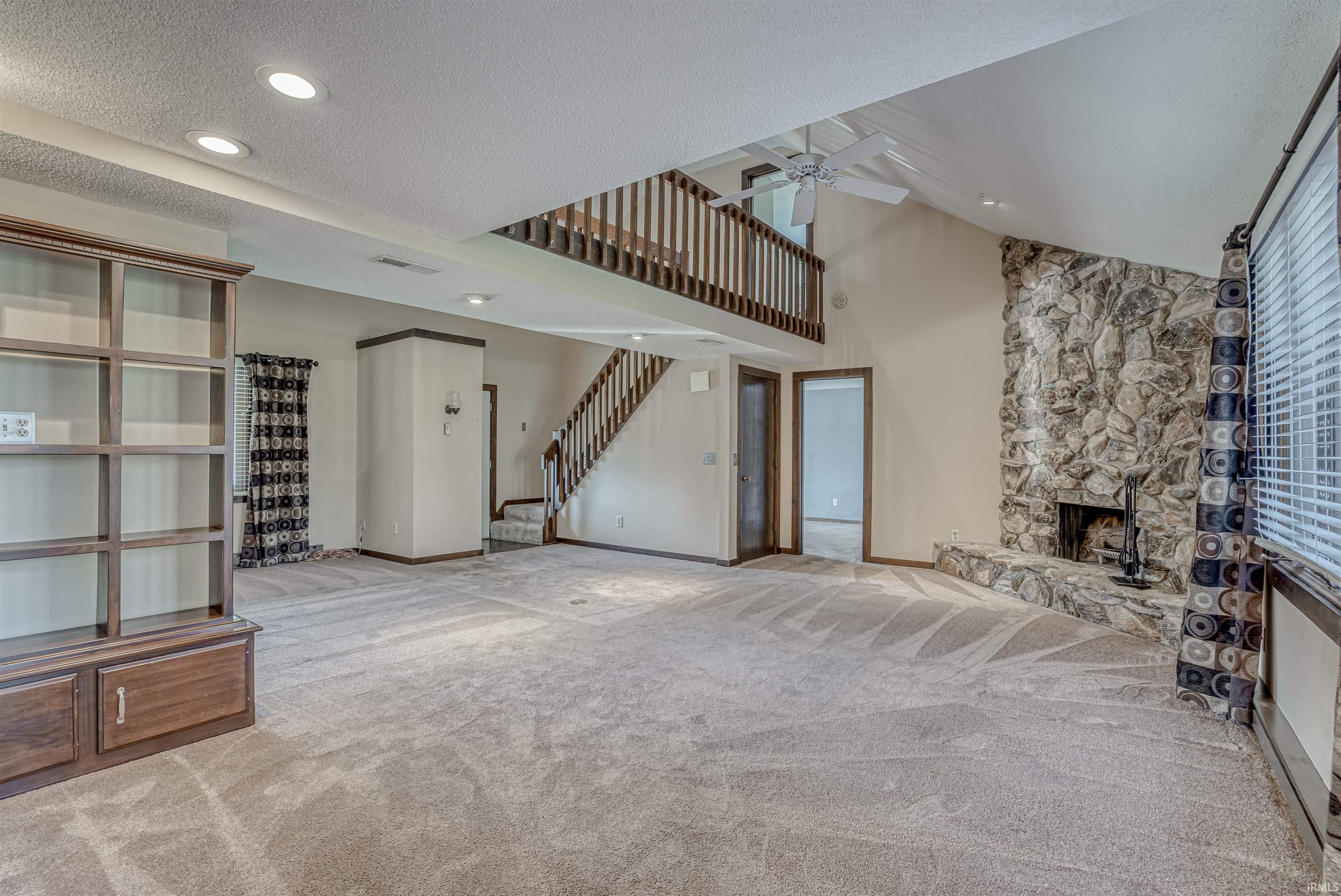 Unfurnished living room with a stone fireplace, light carpet, recessed lighting, ceiling fan, and a high textured ceiling
