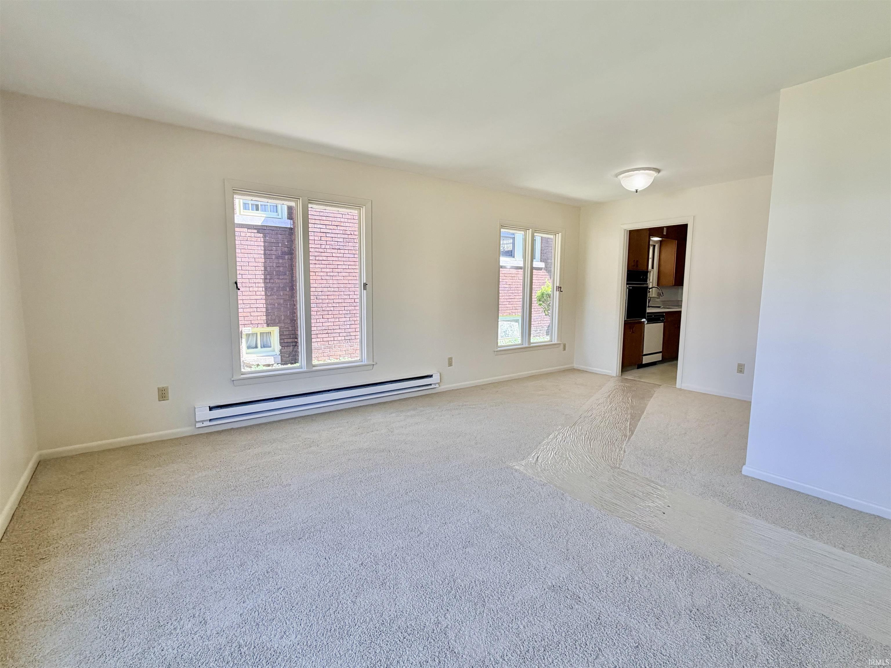Empty room with light colored carpet and baseboard heating