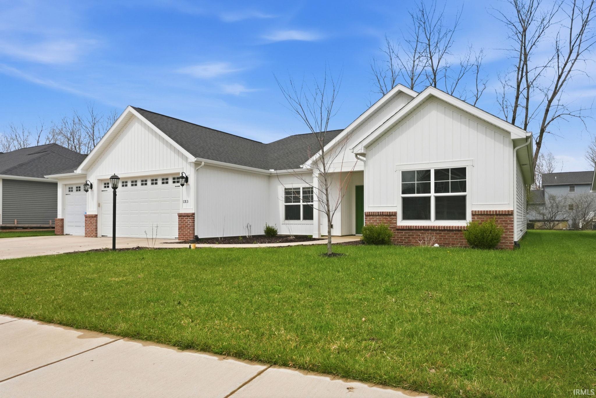 View of front facade with brick siding, an attached garage, concrete driveway, a front lawn, and board and batten siding