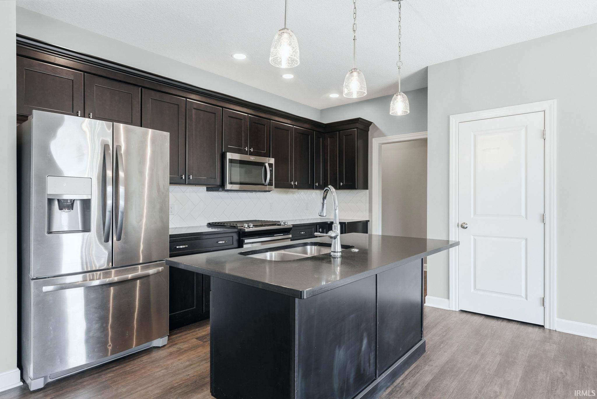 Kitchen with stainless steel appliances, dark wood-style floors, dark stone counters, and decorative backsplash