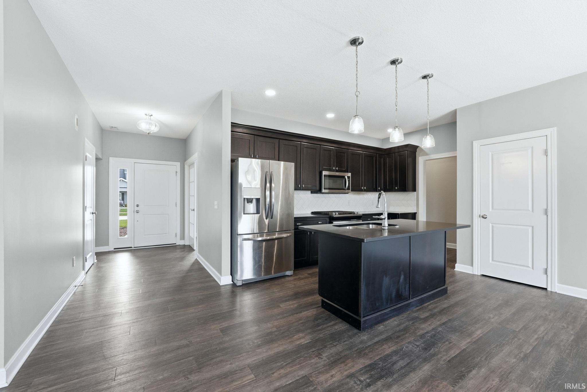 Kitchen featuring stainless steel appliances, an island with sink, pendant lighting, and dark wood finished floors