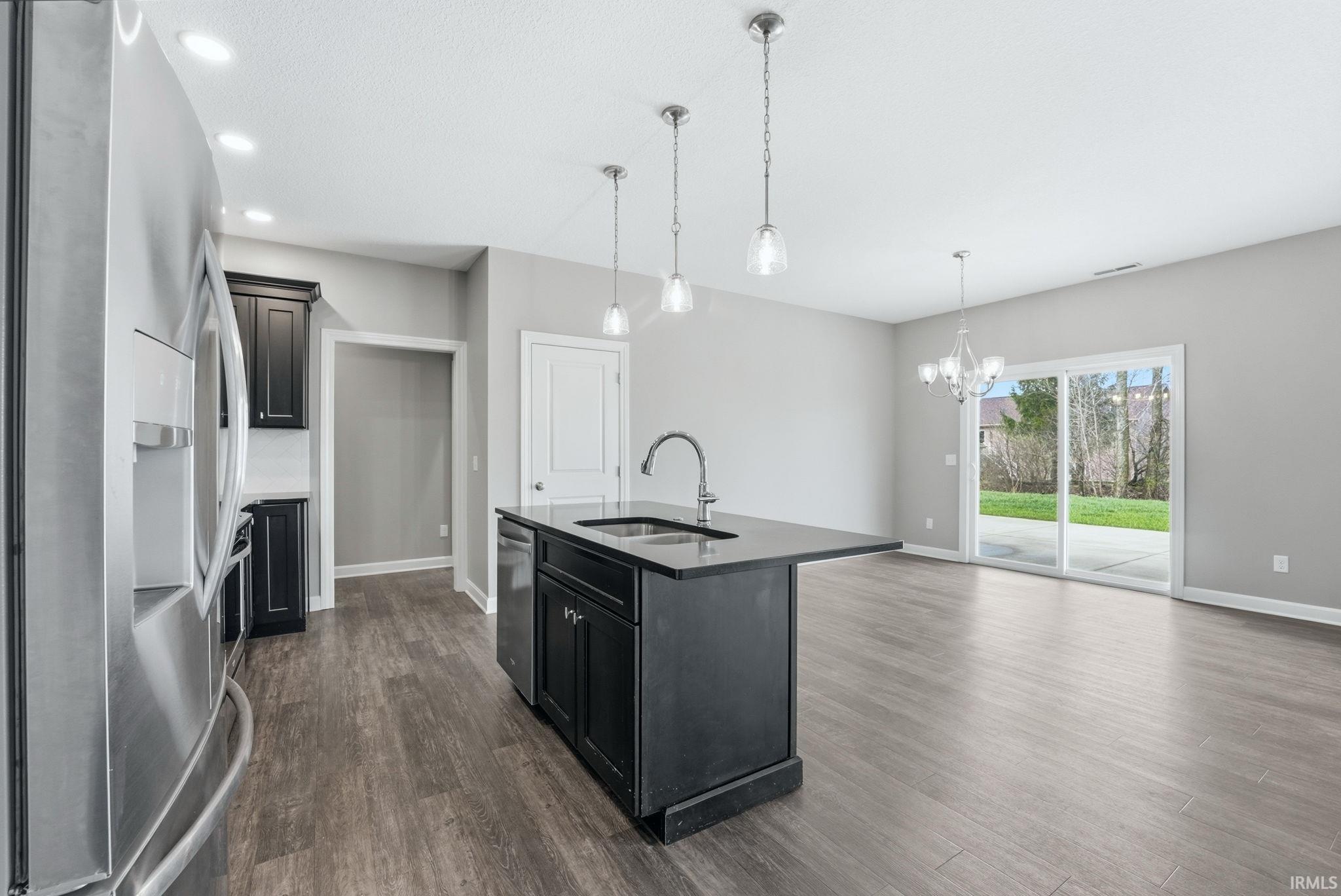 Kitchen featuring stainless steel appliances, dark wood-style floors, a kitchen island with sink, dark stone countertops, and suspended lighting