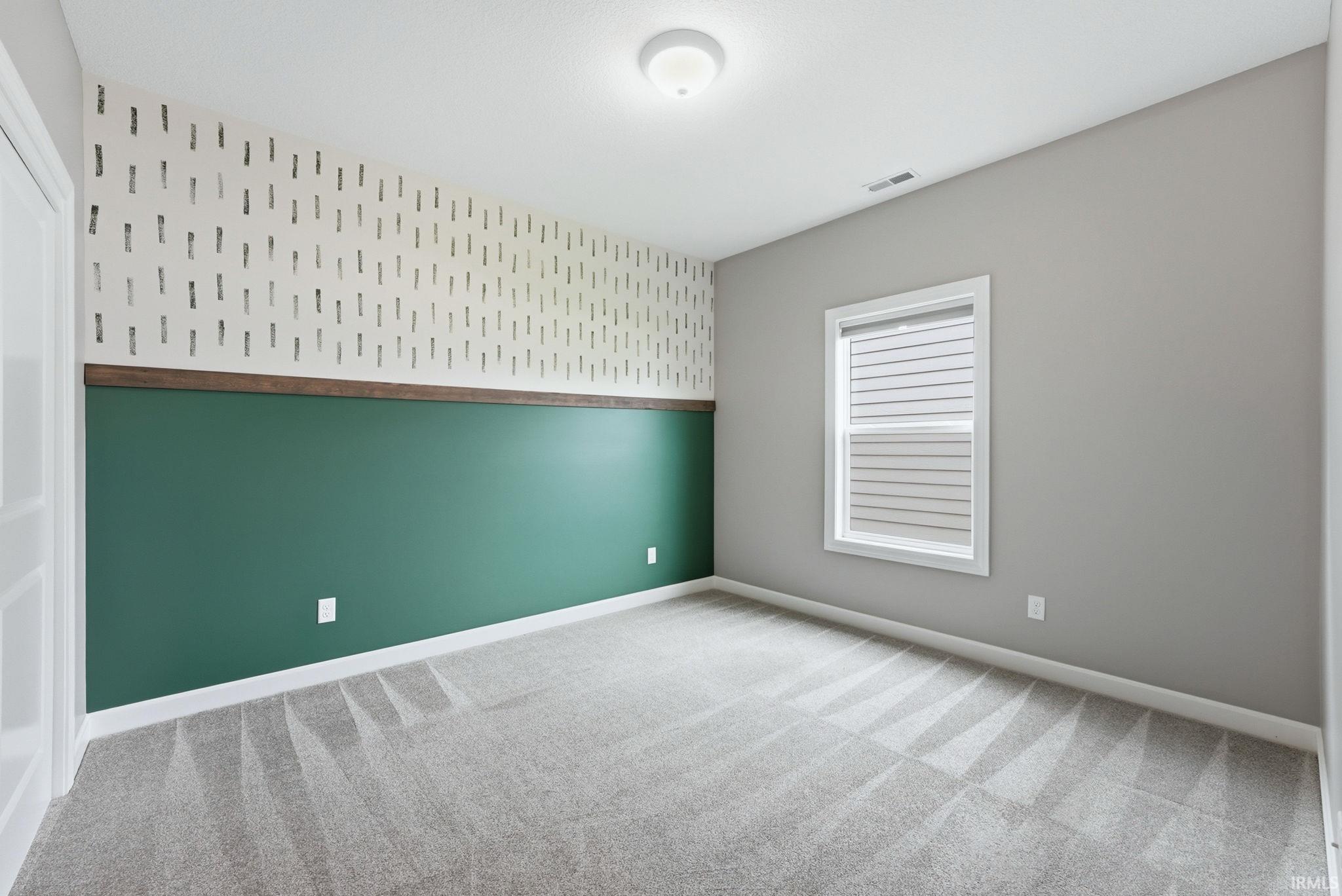 Empty room featuring wallpapered walls, light carpet, and an accent wall