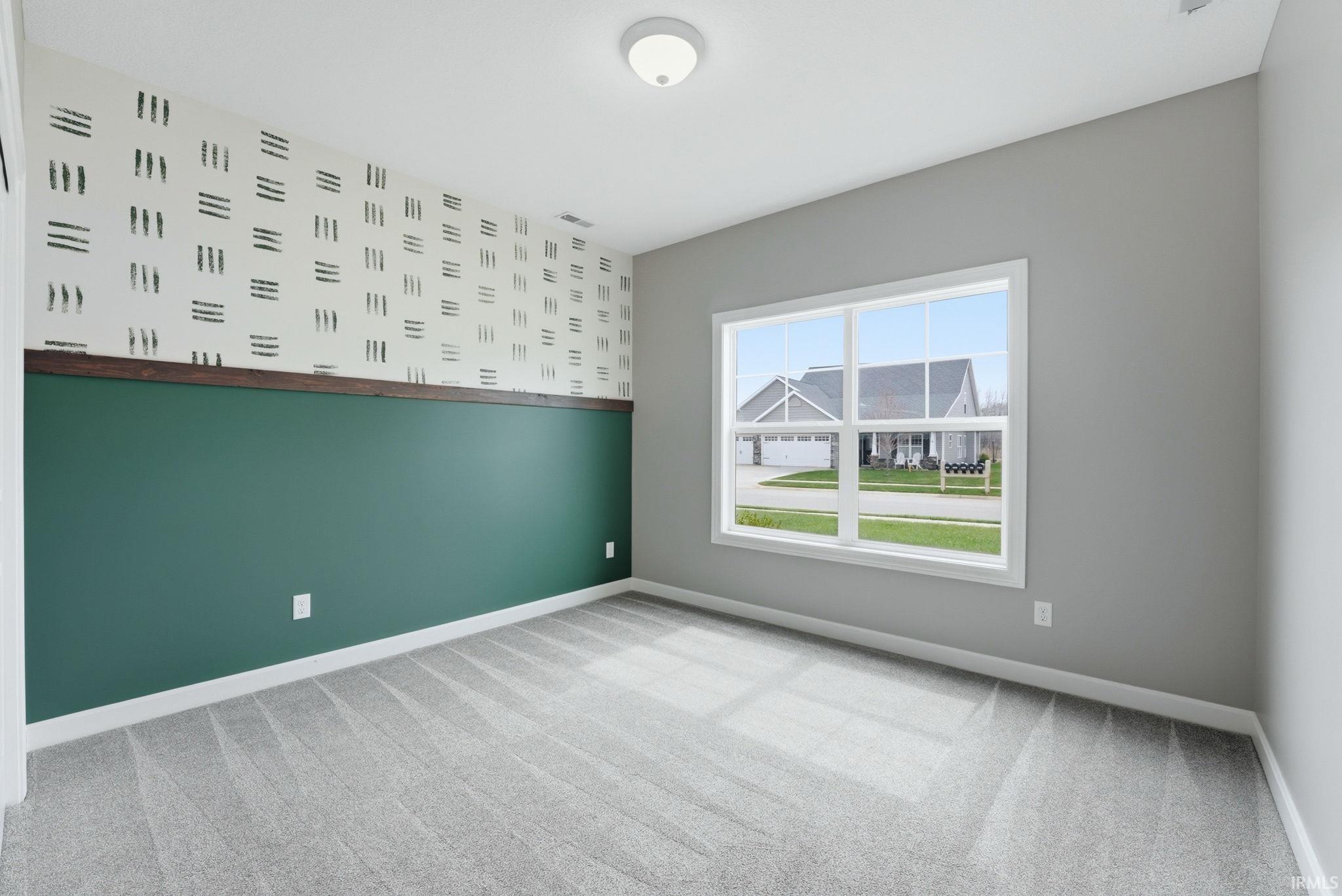 Empty room with light colored carpet, wallpapered walls, and an accent wall