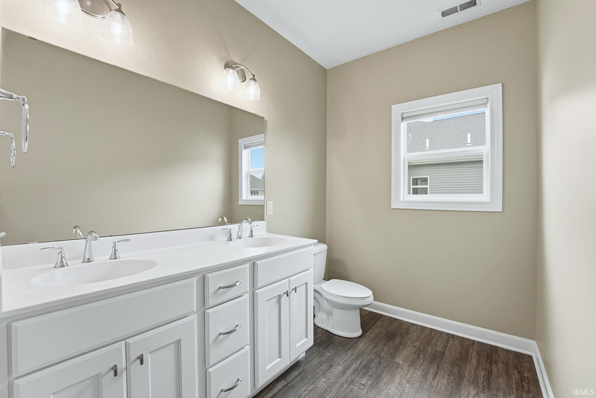 Full bathroom featuring double vanity and dark wood-style flooring