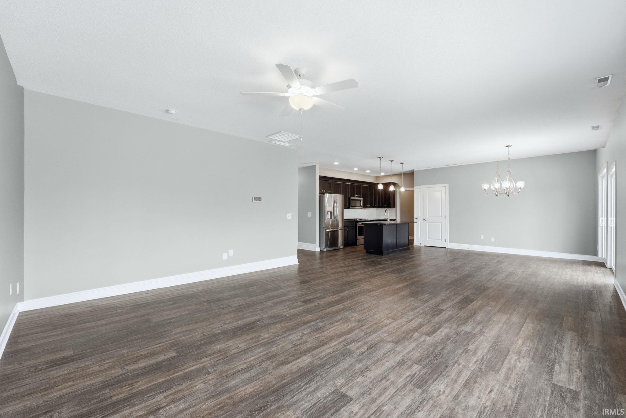 Unfurnished living room featuring ceiling fan, a chandelier, and dark wood-style flooring