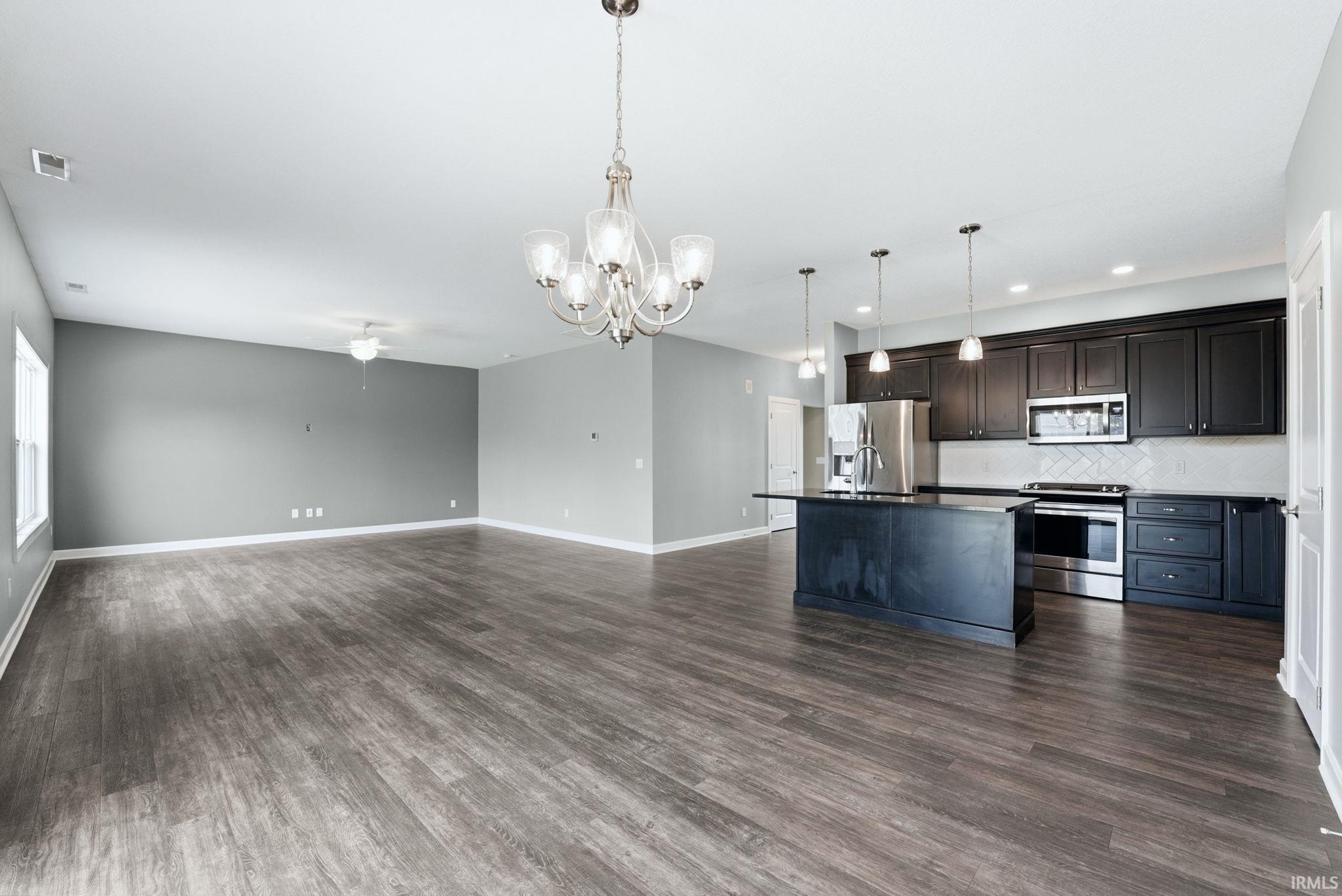 Kitchen with open floor plan, stainless steel appliances, a kitchen island with sink, hanging lights, and decorative backsplash