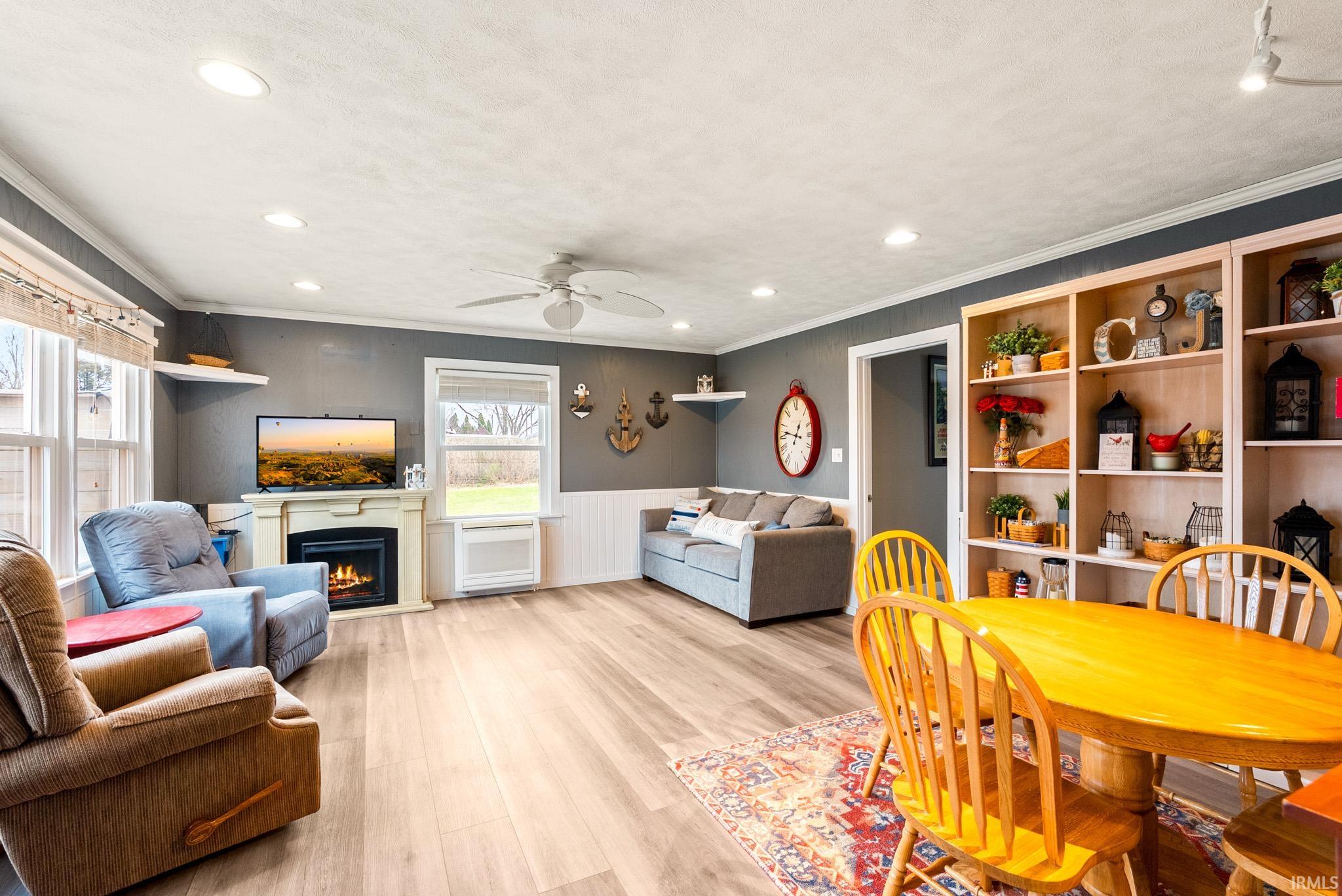 Dining space with wainscoting, light wood finished floors, a lit fireplace, a ceiling fan, and crown molding