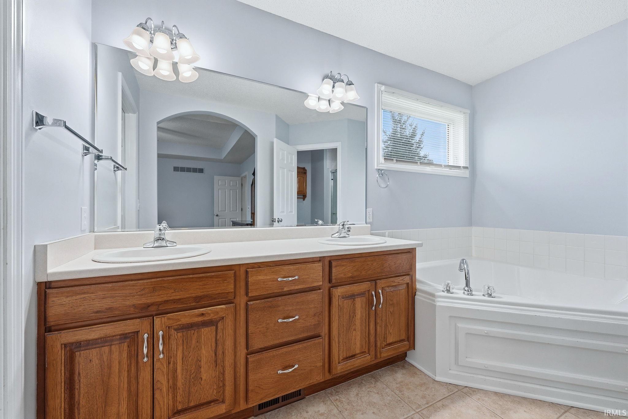 Full bathroom with double vanity, a bath, light tile patterned floors, and a chandelier