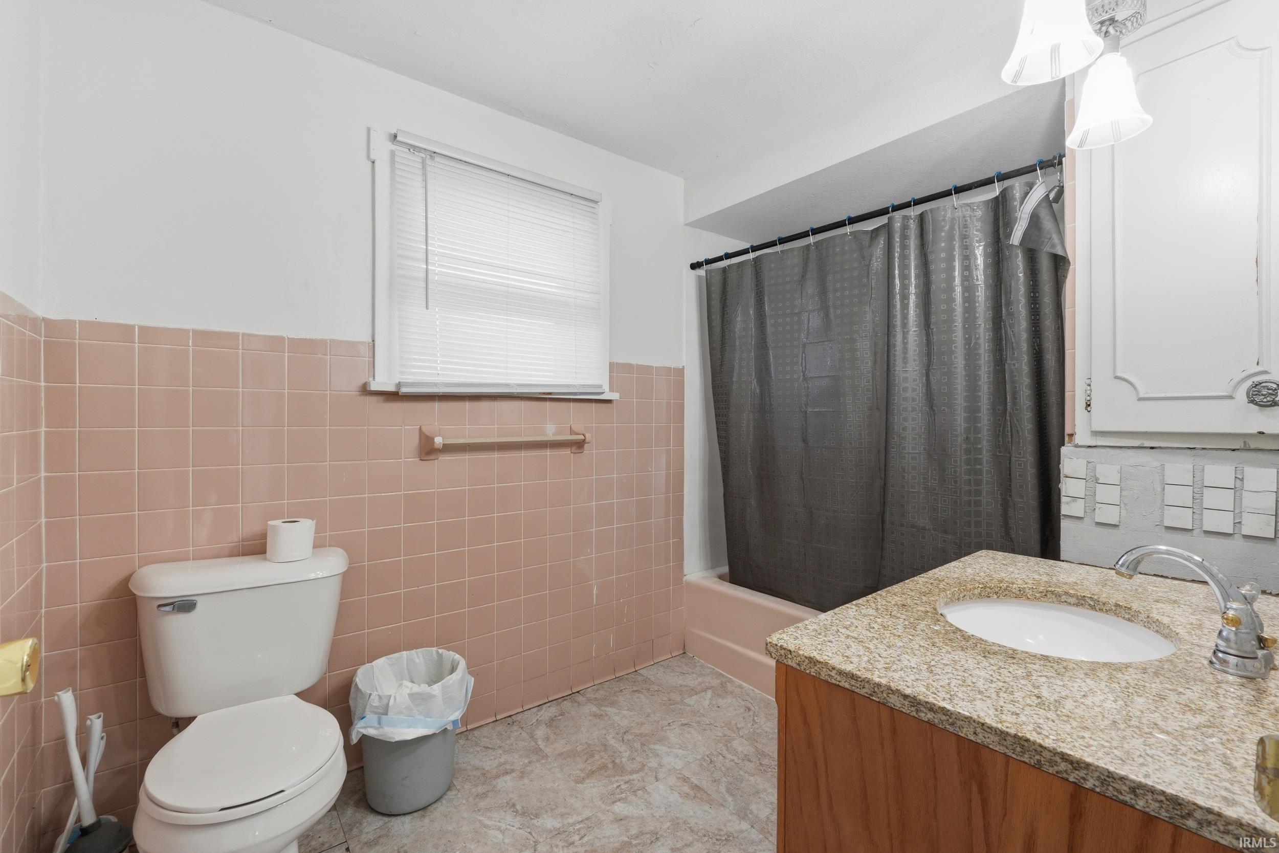 Full bathroom featuring vanity, shower / bath combination with curtain, a wainscoted wall, and tile walls