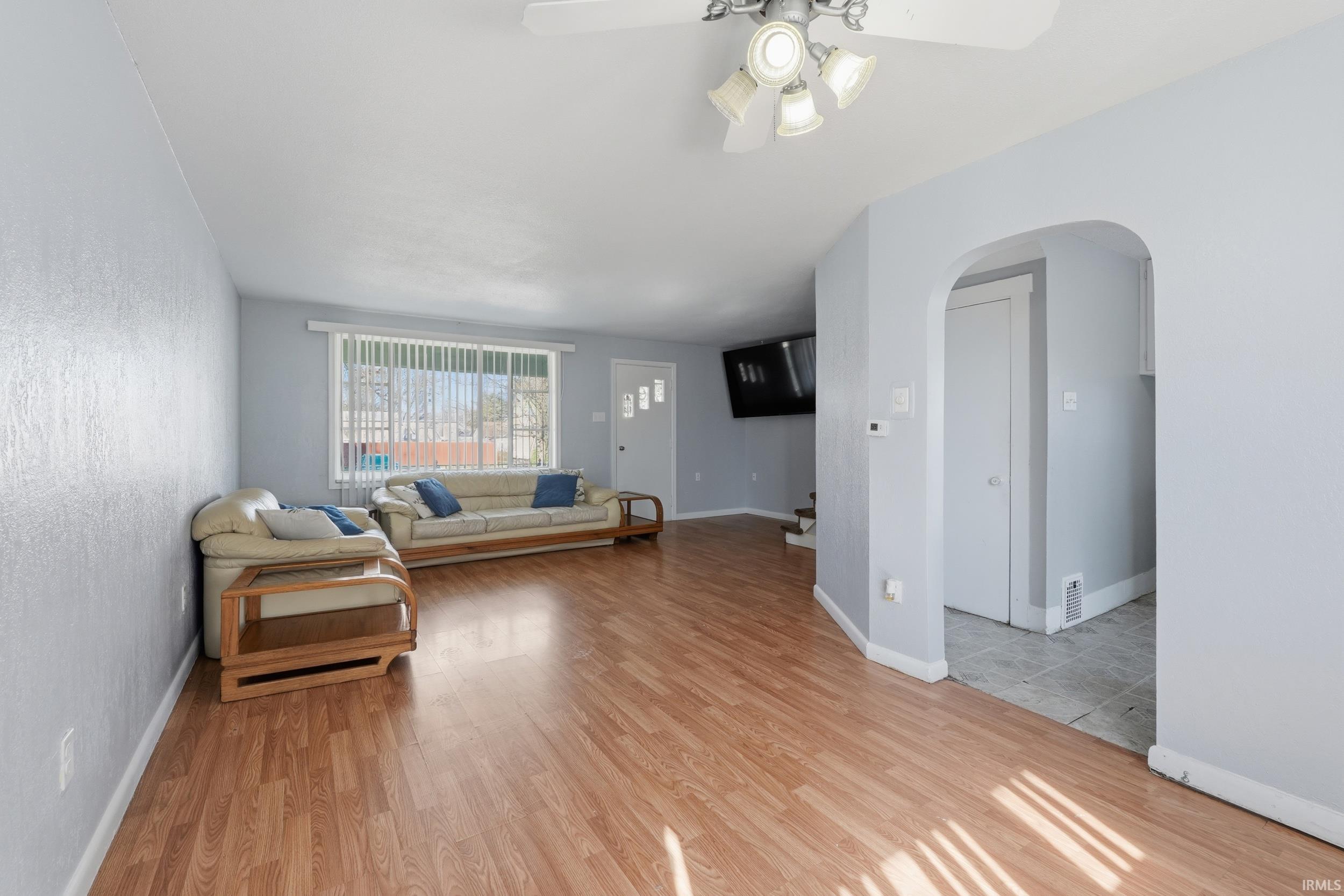 Living room with light wood-type flooring, a ceiling fan, and arched walkways