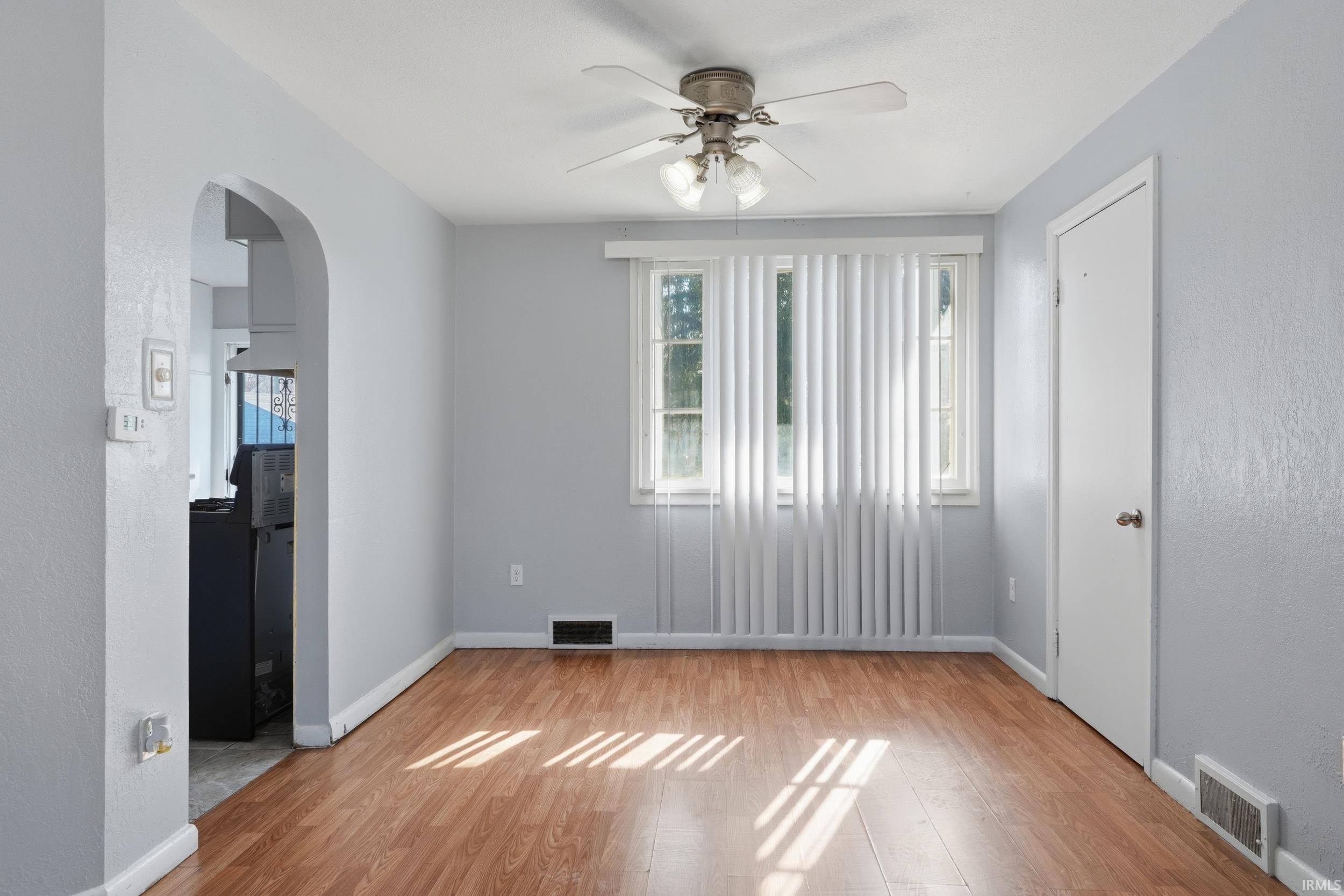 Empty room featuring ceiling fan, arched walkways, healthy amount of natural light, light wood-type flooring, and a textured wall