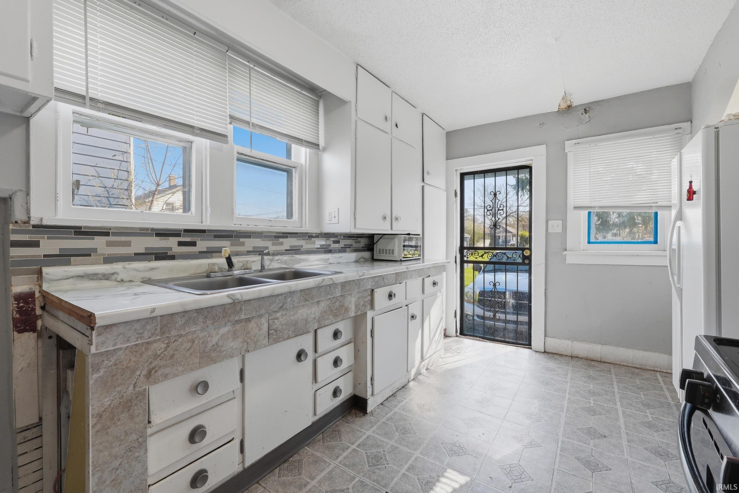 Kitchen featuring white cabinetry, light countertops, stainless steel range with gas stovetop, white fridge with ice dispenser, and tasteful backsplash