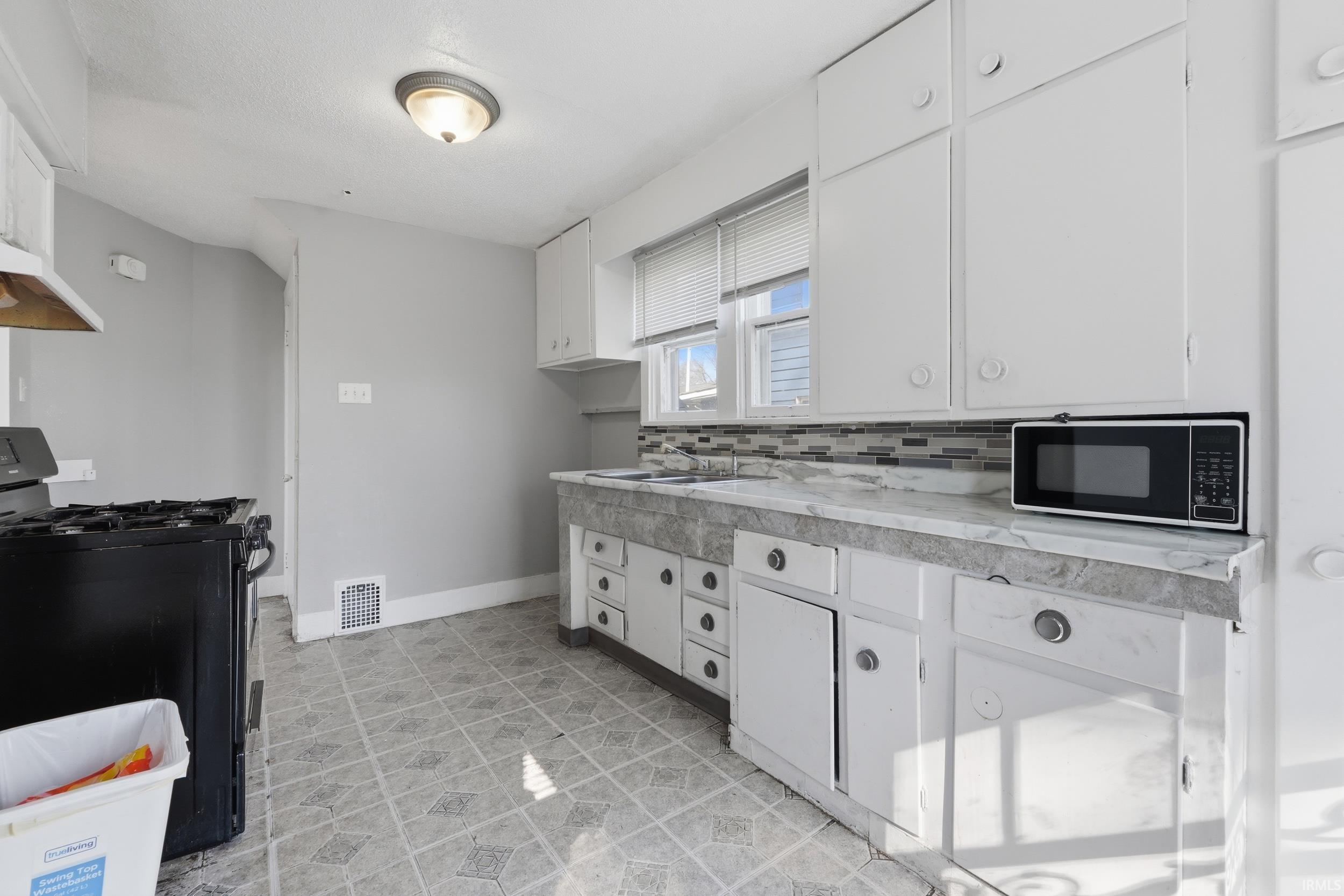 Kitchen with black range with gas stovetop, white cabinetry, light countertops, stainless steel microwave, and tasteful backsplash