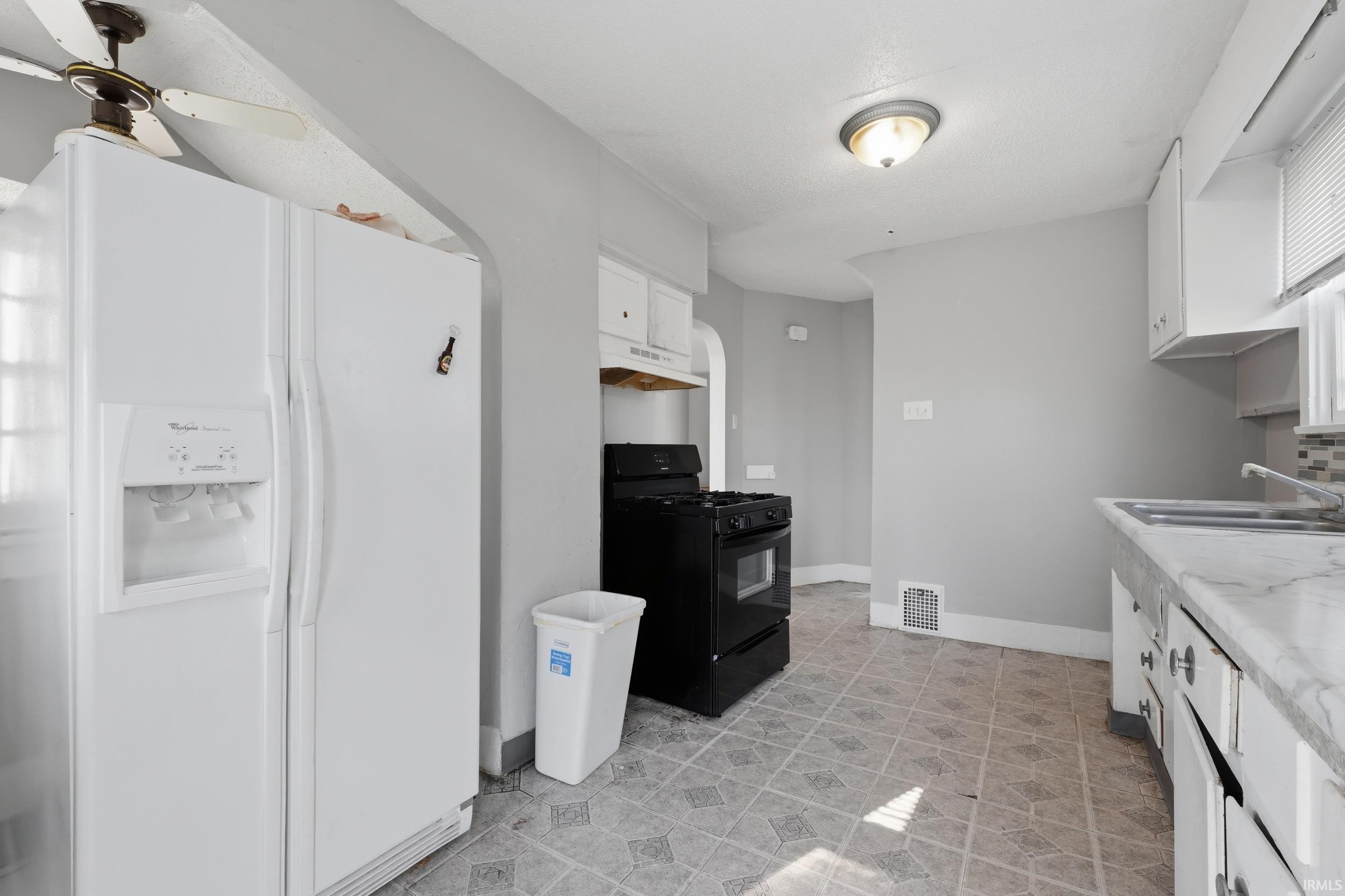 Kitchen with white fridge with ice dispenser, black range with gas cooktop, white cabinets, light countertops, and a ceiling fan
