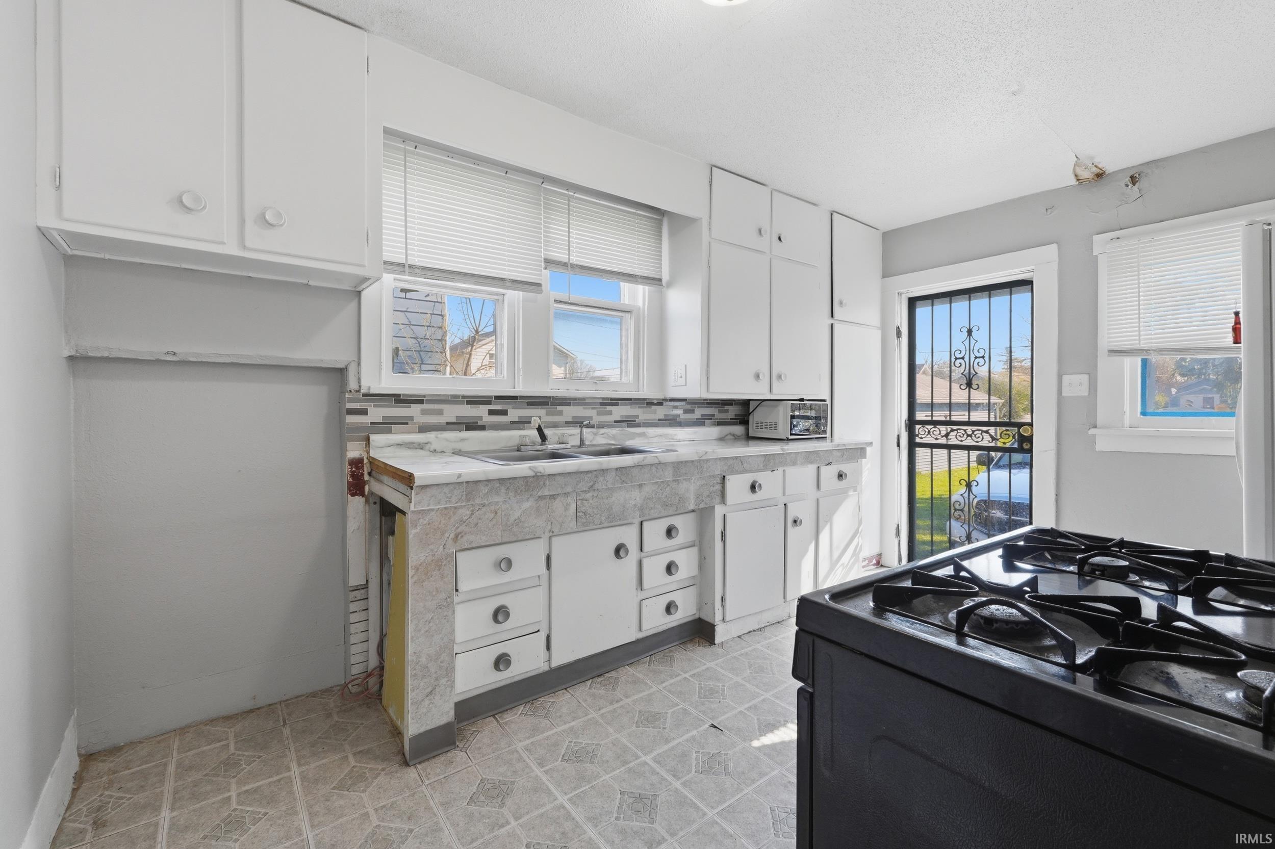 Kitchen with black gas range, white cabinetry, light countertops, backsplash, and freestanding refrigerator