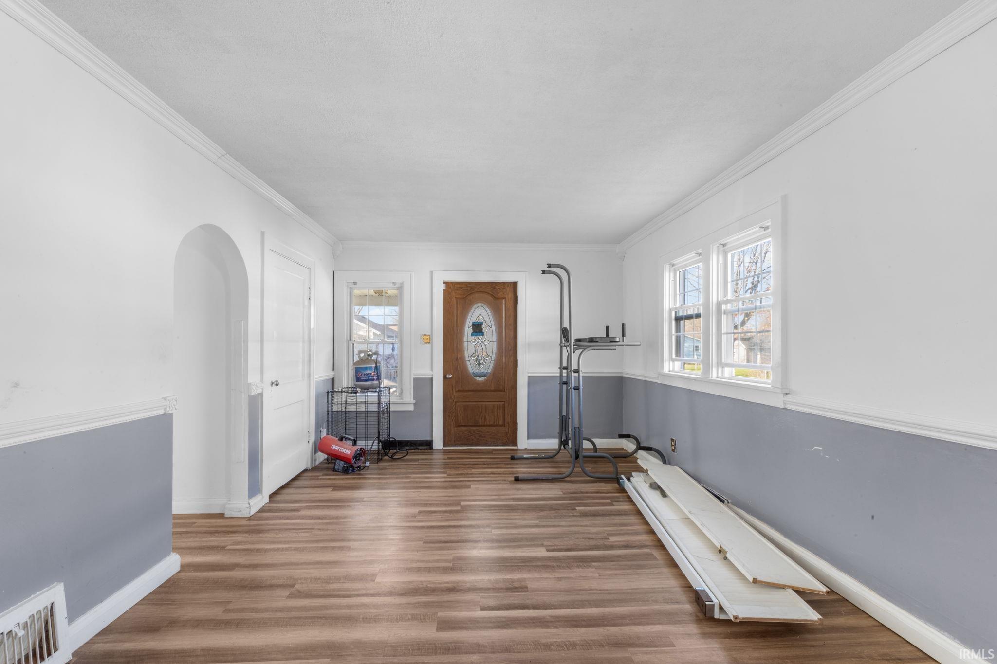 Entrance foyer with arched walkways, dark wood-type flooring, and crown molding