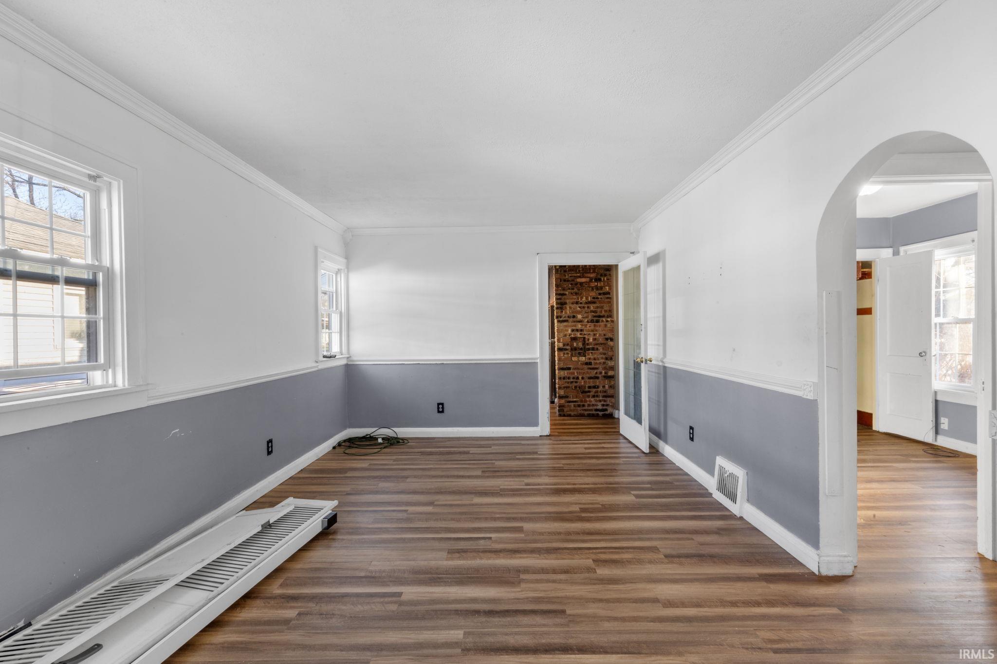 Living room with arched walkways, dark wood-type flooring, and crown molding