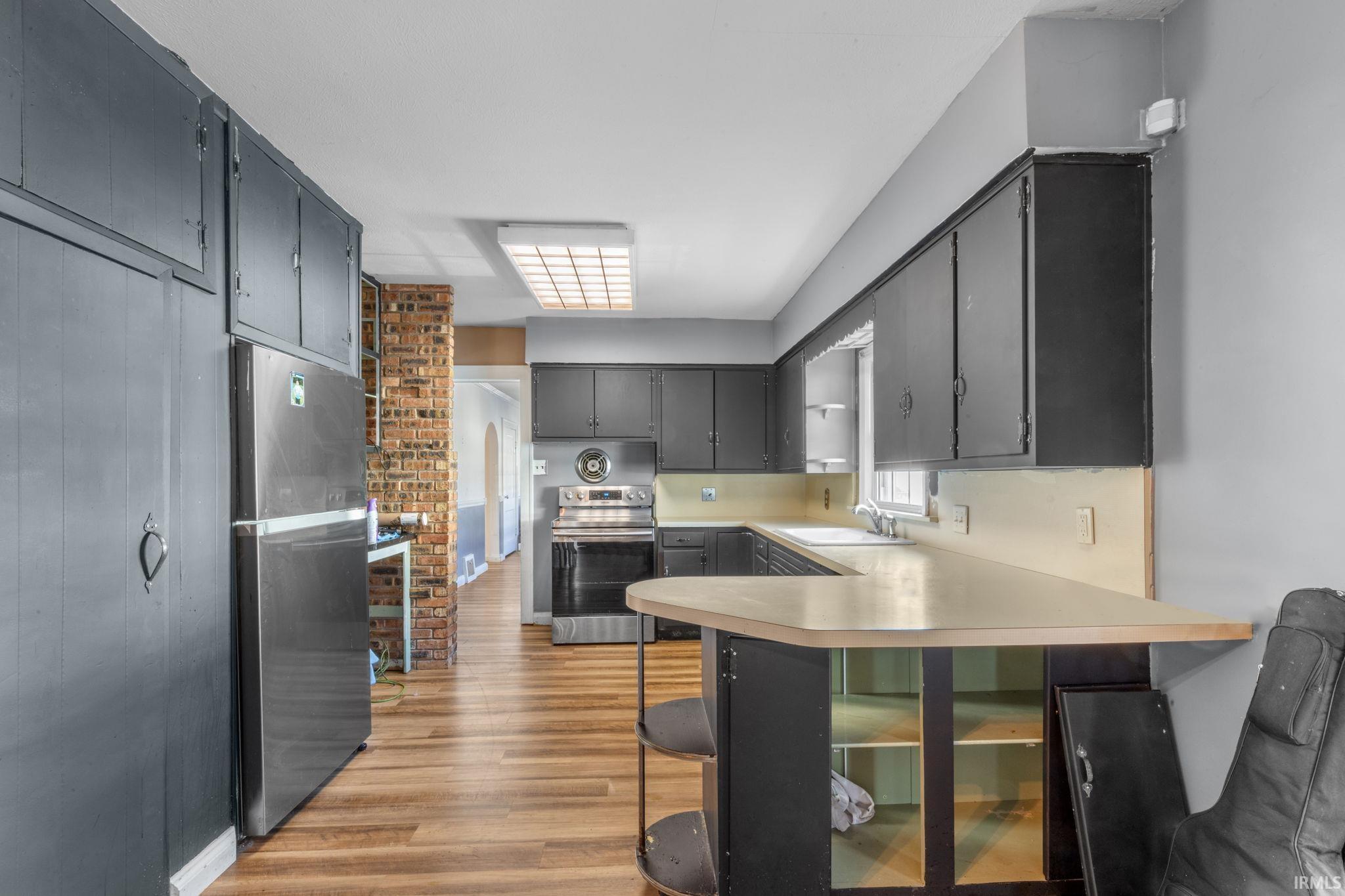 Kitchen featuring a breakfast bar, a peninsula, light countertops, stainless steel appliances, and dark wood-type flooring