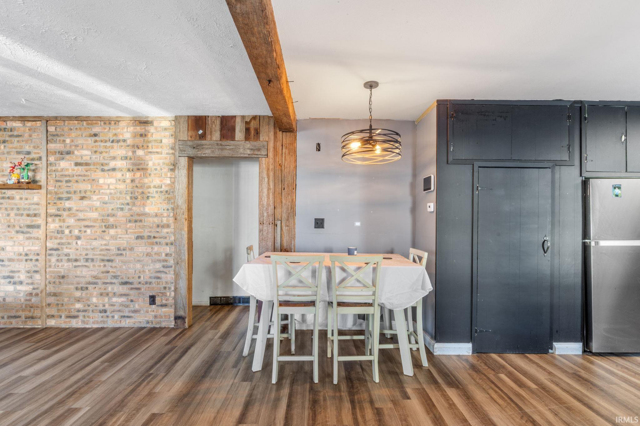 Dining area with beamed ceiling, dark wood-style flooring, brick wall, and hanging lights