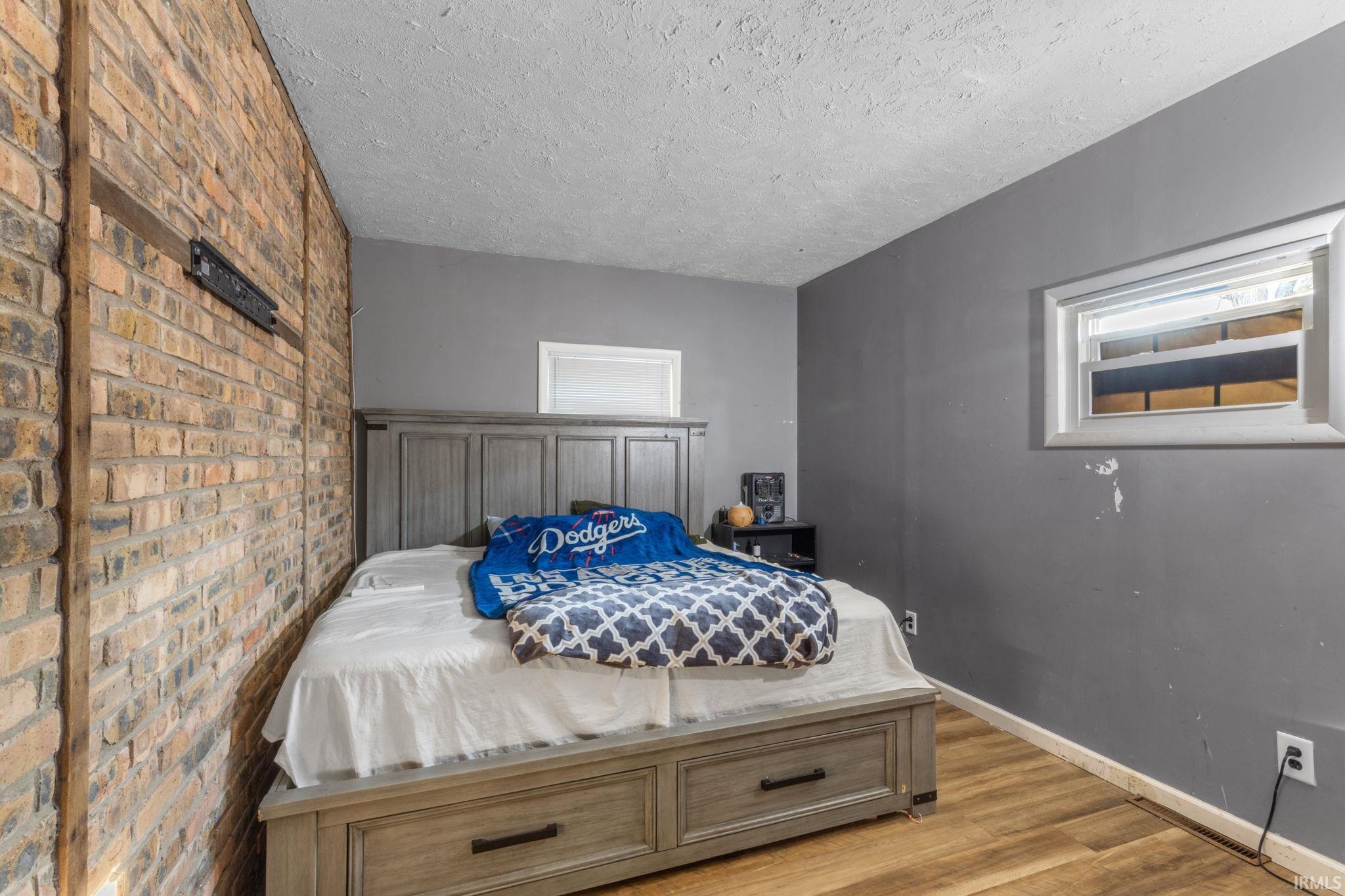 Bedroom featuring light wood-style floors, brick wall, and a textured ceiling