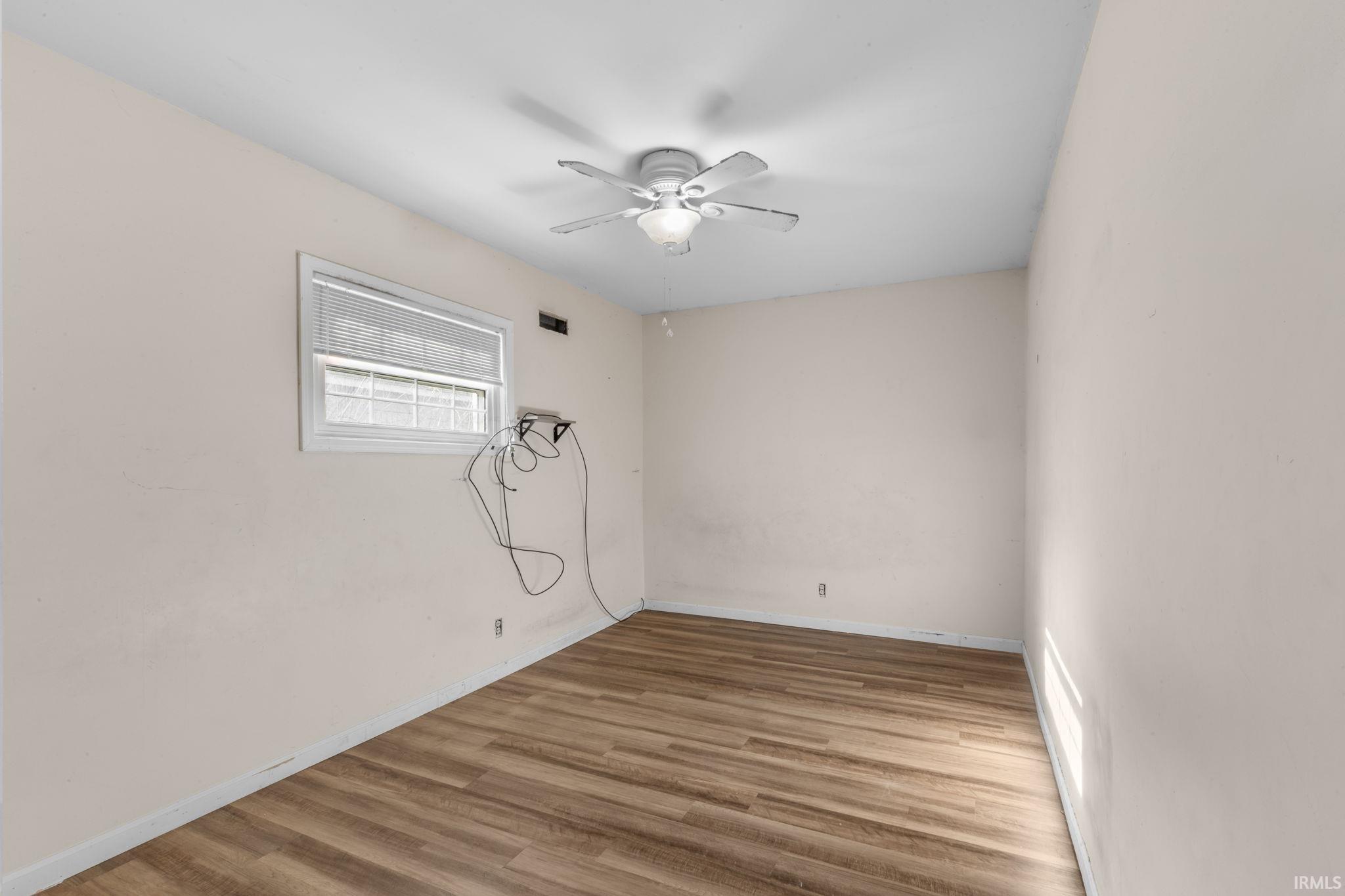 Empty room featuring wood finished floors, a ceiling fan, and a baseboard heating unit
