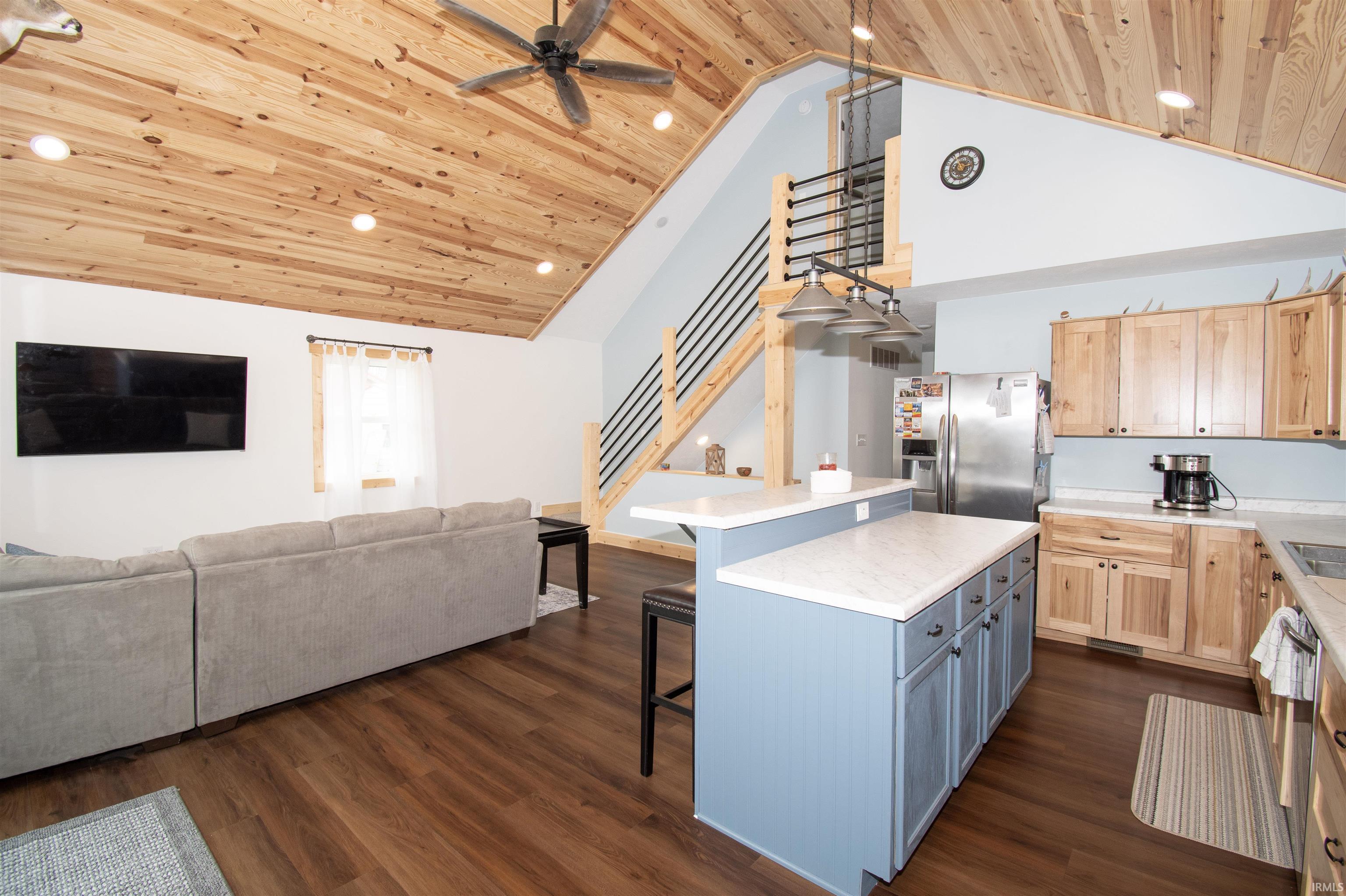 Two tone kitchen with a breakfast bar area, light countertops, a high wood ceiling, stainless steel fridge, and open floor plan