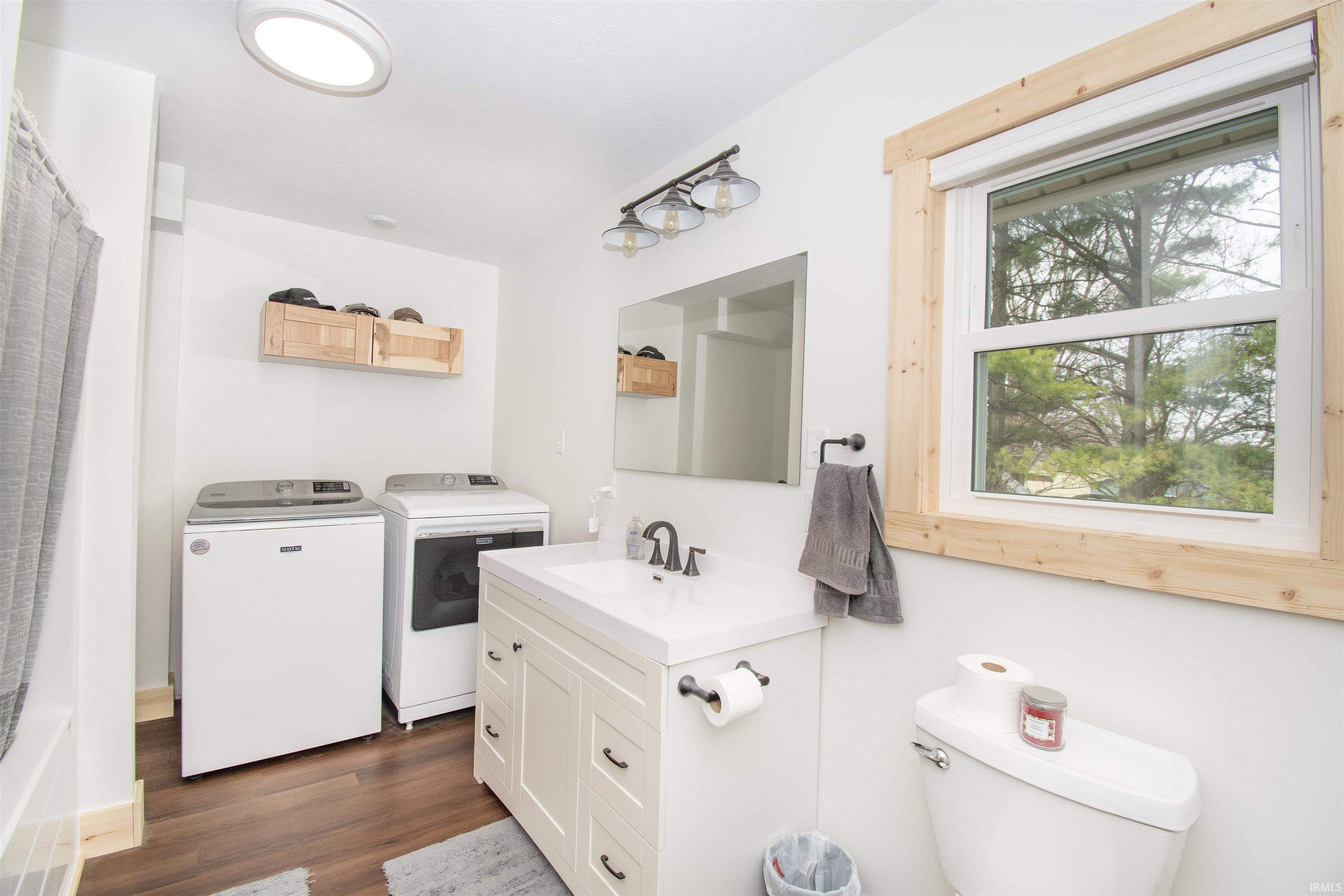 Full bathroom with vanity, washing machine and dryer, dark wood-style floors, and shower / bathtub combination with curtain