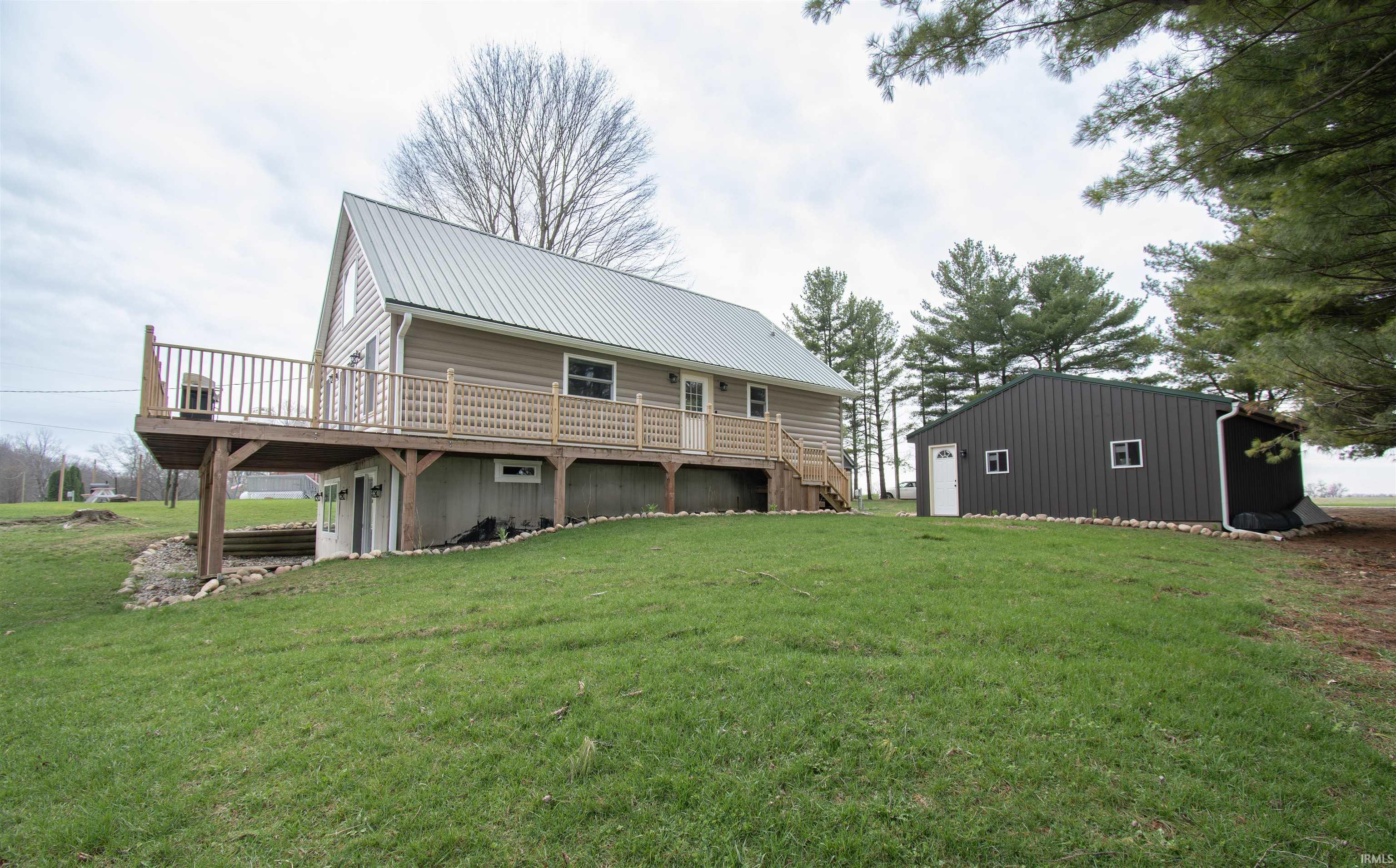 Back of property with a wooden deck, a yard, an outbuilding, and a metal roof