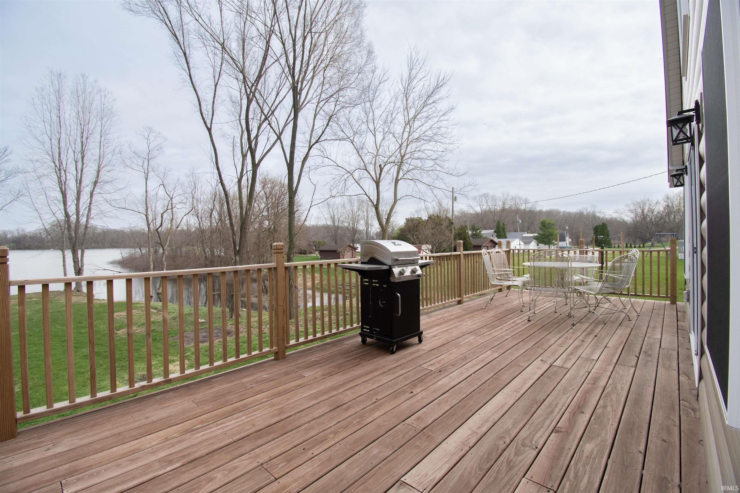 Wooden deck with area for grilling, a lawn, a water view, and outdoor dining space