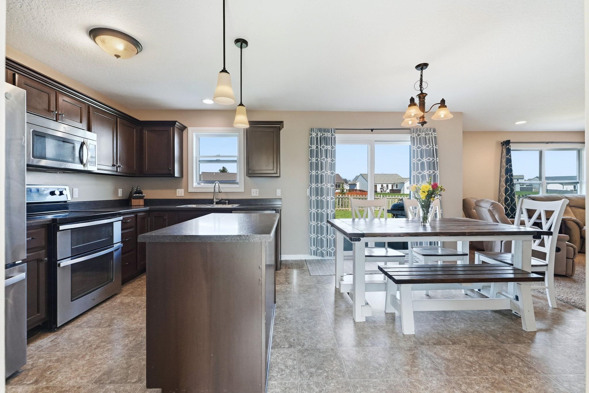 Kitchen with dark wood finish cabinets, stainless steel appliances, dark countertops, a kitchen island, and suspended lighting
