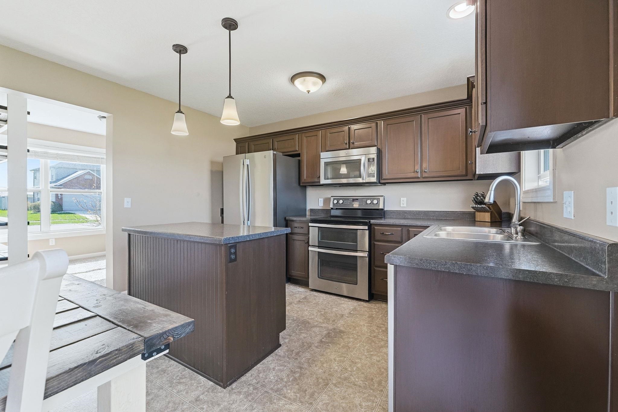 Kitchen featuring dark countertops, stainless steel appliances, dark wood finish cabinetry, and a center island