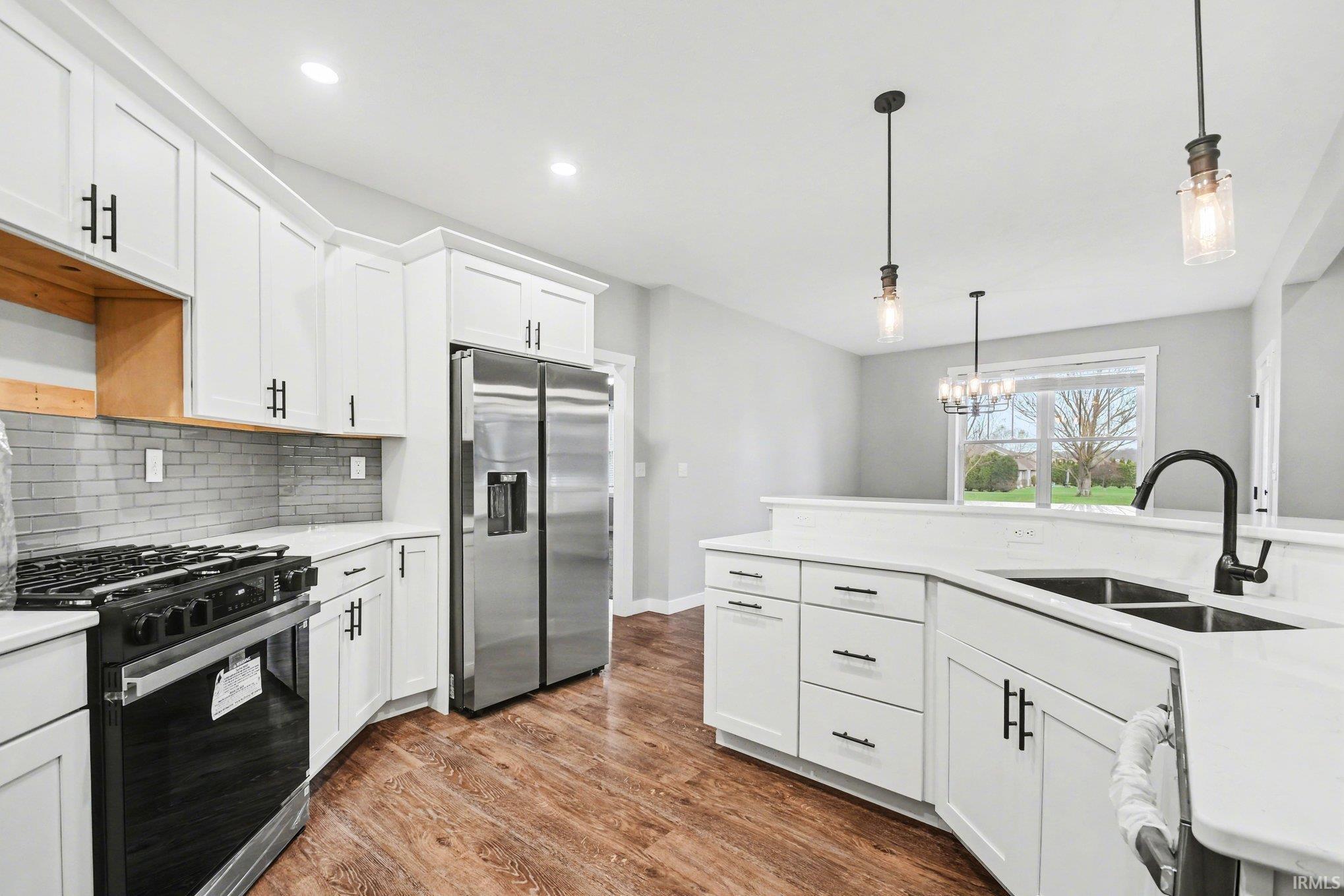 Kitchen featuring black gas stove, white cabinets, stainless steel fridge, dark wood-style flooring, and light stone counters