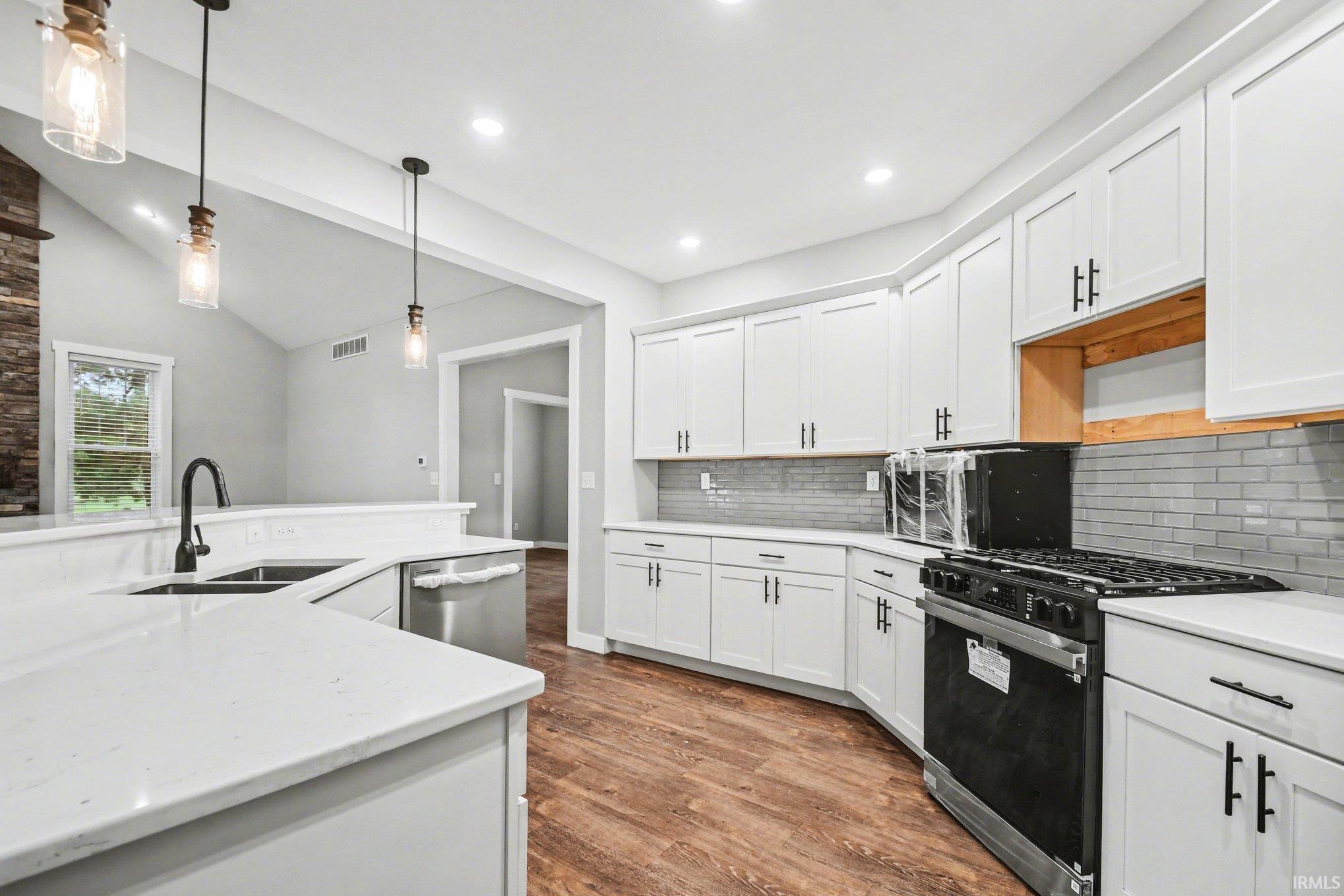 Kitchen featuring black gas stove, dark wood-style flooring, white cabinets, vaulted ceiling, and hanging light fixtures