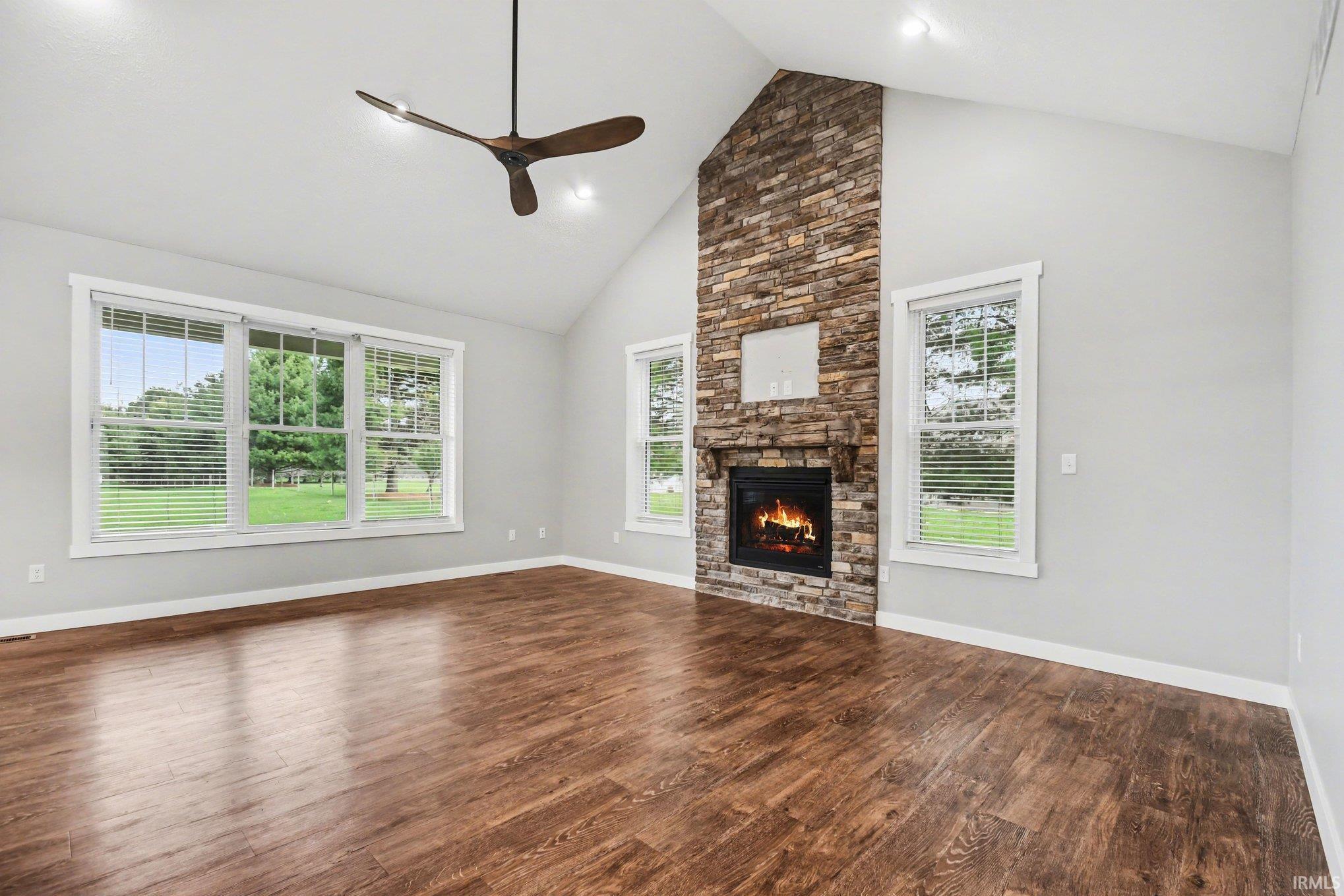Unfurnished living room with ceiling fan, a high ceiling, dark wood-style flooring, and a stone fireplace