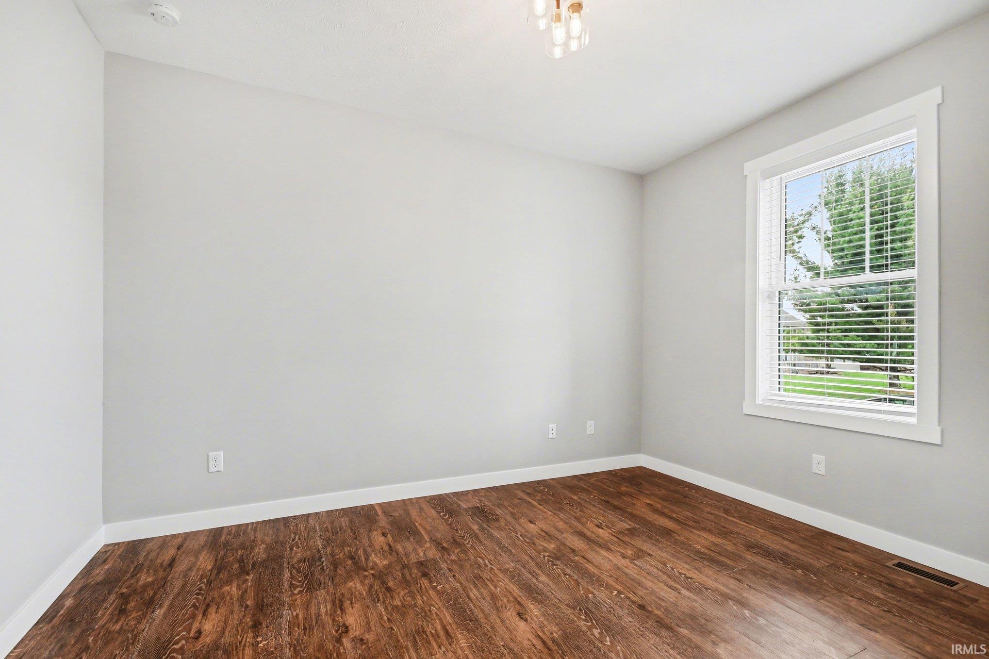 Empty room with dark wood-type flooring and baseboards