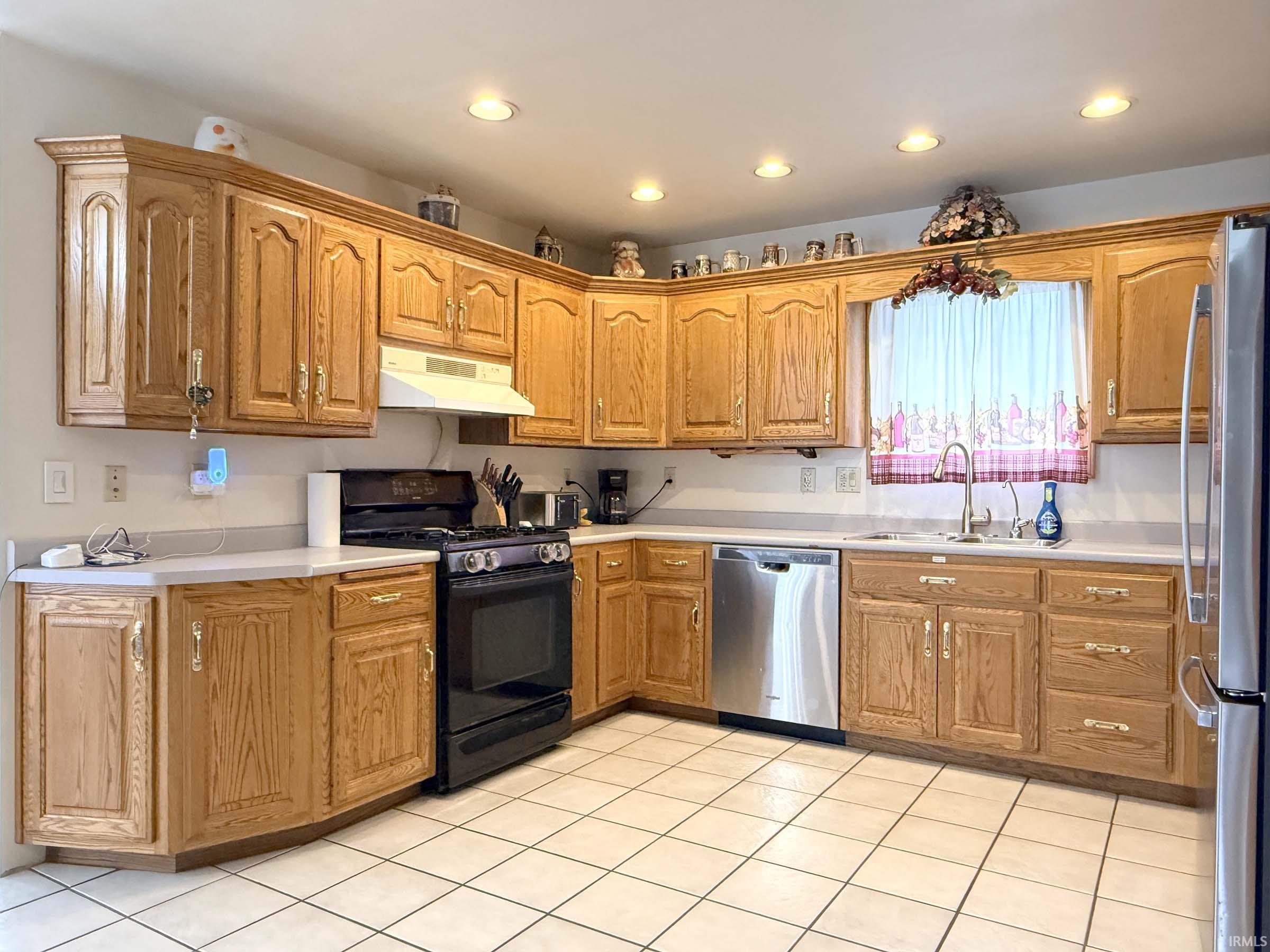 Kitchen with stainless steel appliances, light countertops, recessed lighting, light tile patterned floors, and wood finish cabinets
