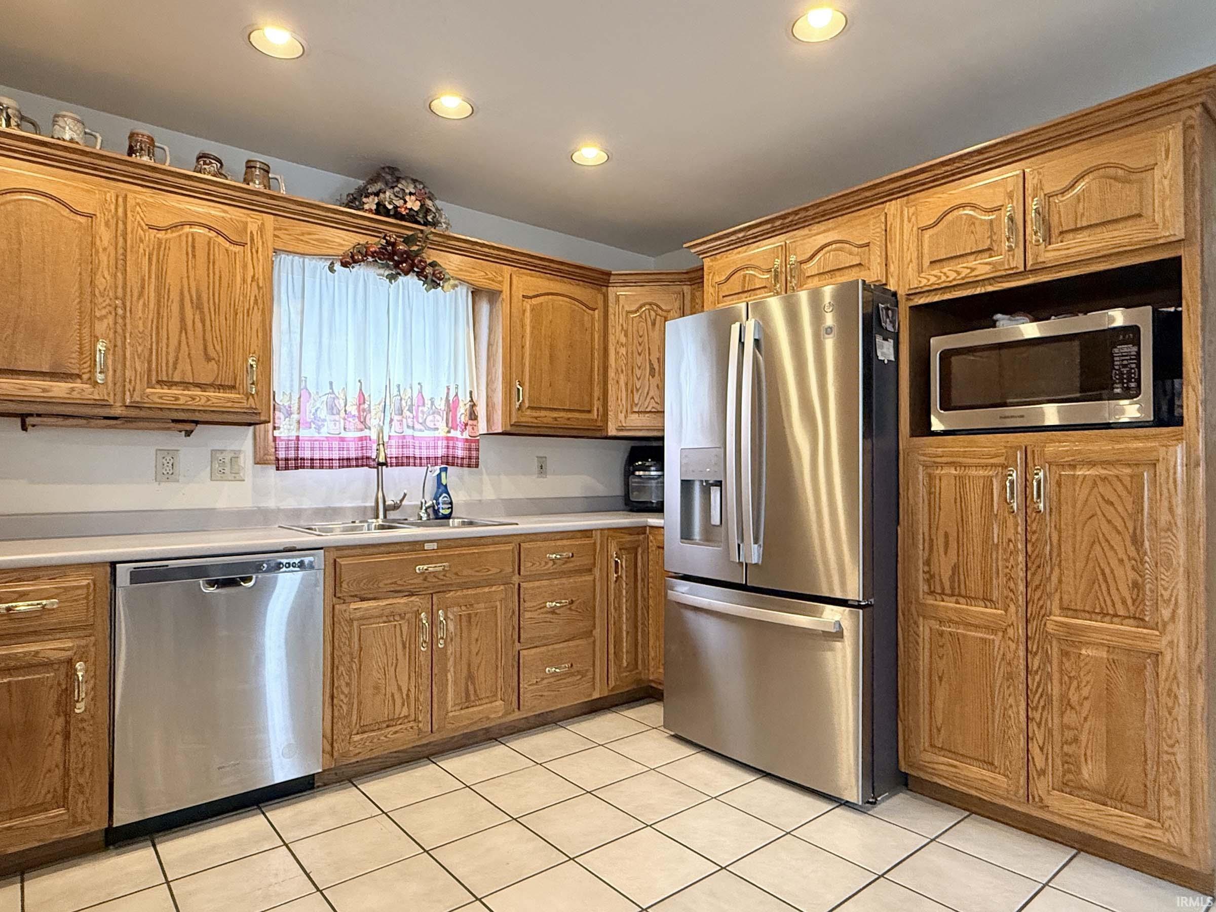 Kitchen featuring stainless steel appliances, light countertops, wood finish cabinets, light tile patterned flooring, and recessed lighting