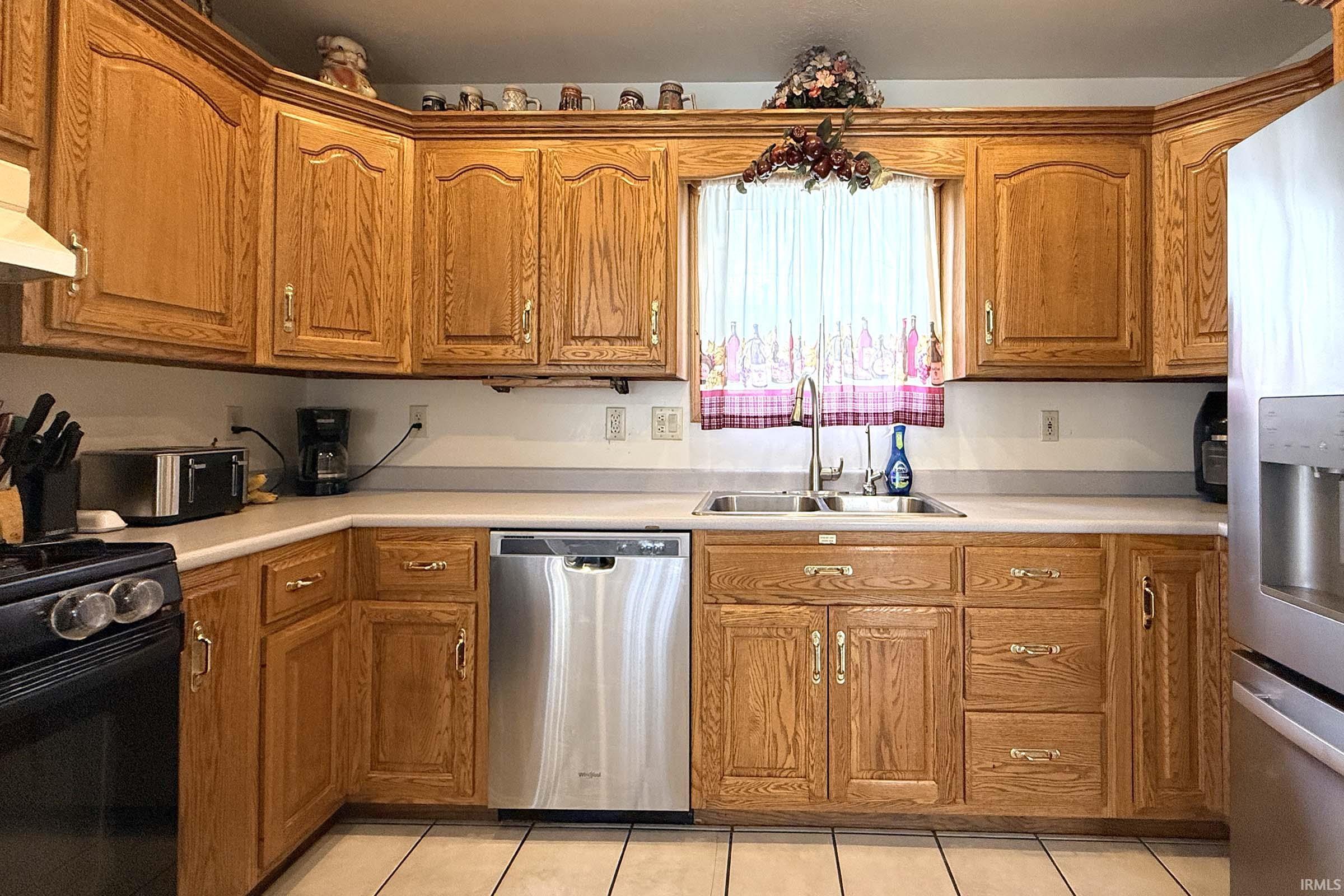 Kitchen with stainless steel appliances, wood finish cabinets, light countertops, and light tile patterned floors