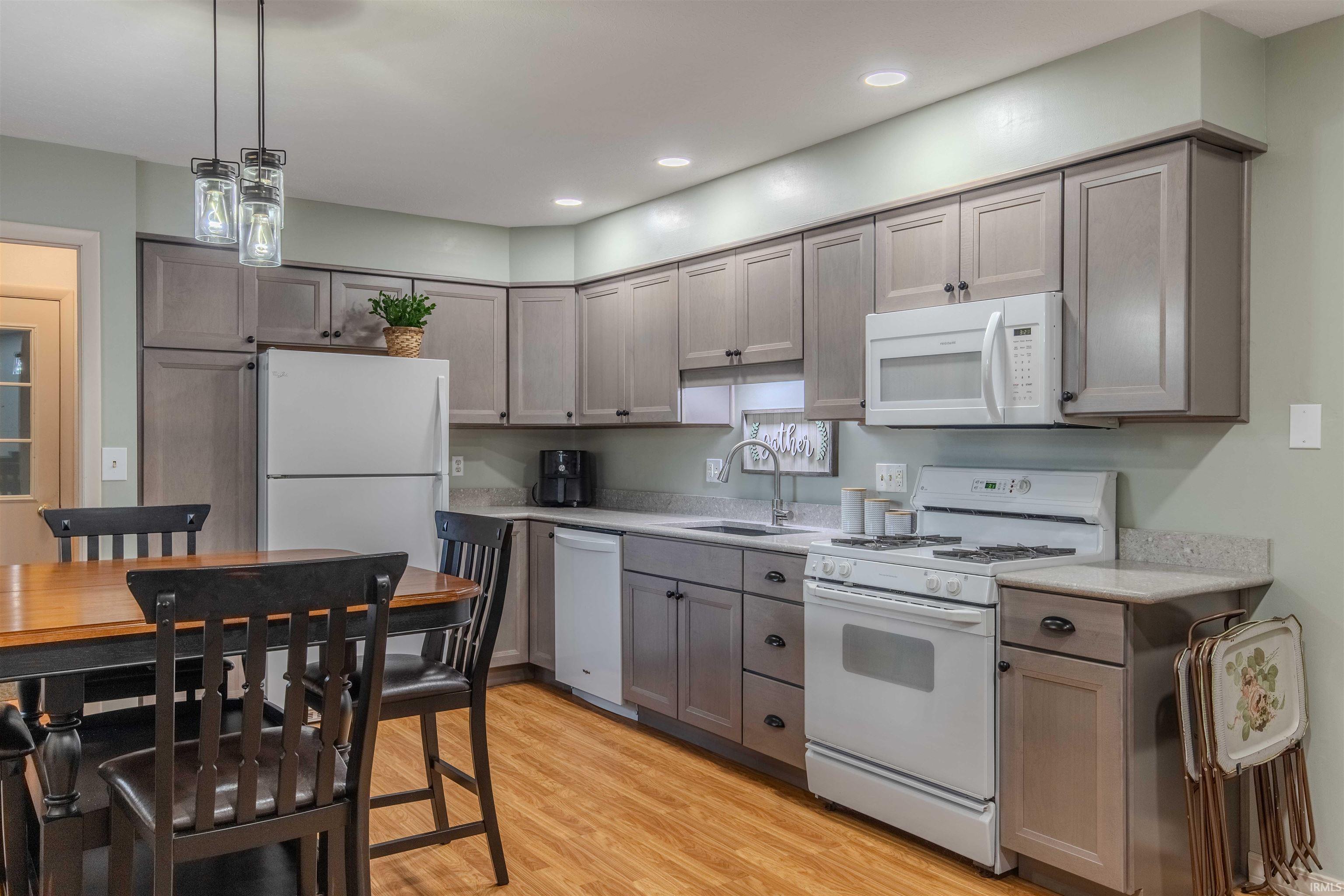 Kitchen with white appliances, light wood-type flooring, pendant lighting, gray cabinetry, and light stone counters