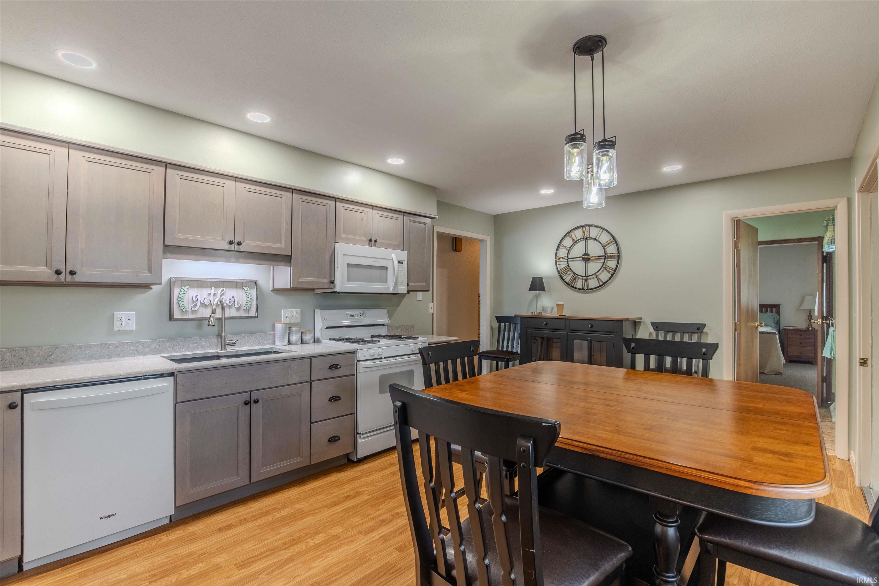 Kitchen with white appliances, hanging light fixtures, light wood finished floors, gray cabinets, and light stone counters
